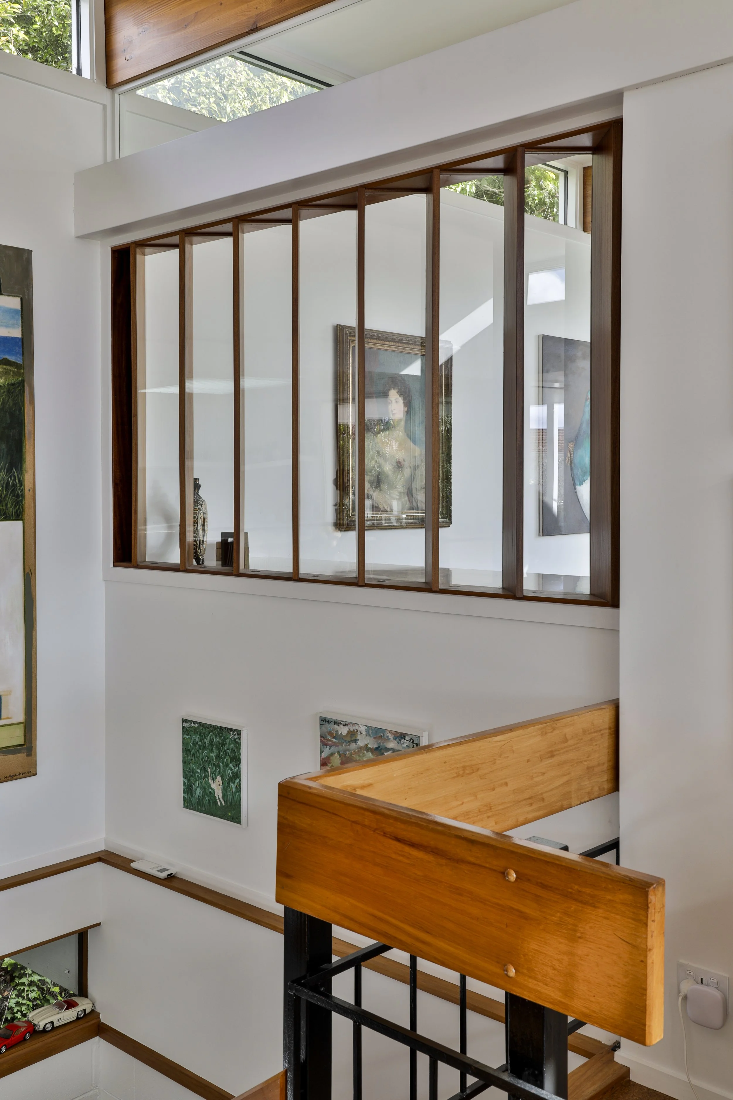 Interior view of a modern home with a wooden staircase, a glass window, and wall art, including paintings and sculptures.