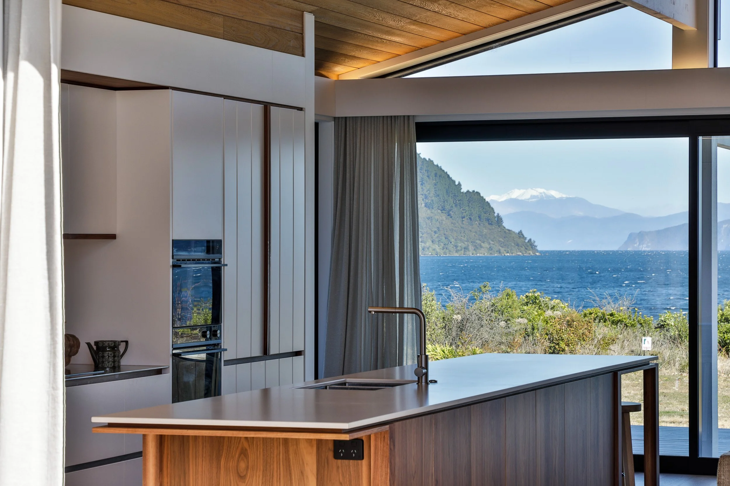 Modern kitchen with large glass sliding door overlooking lake and mountains.
