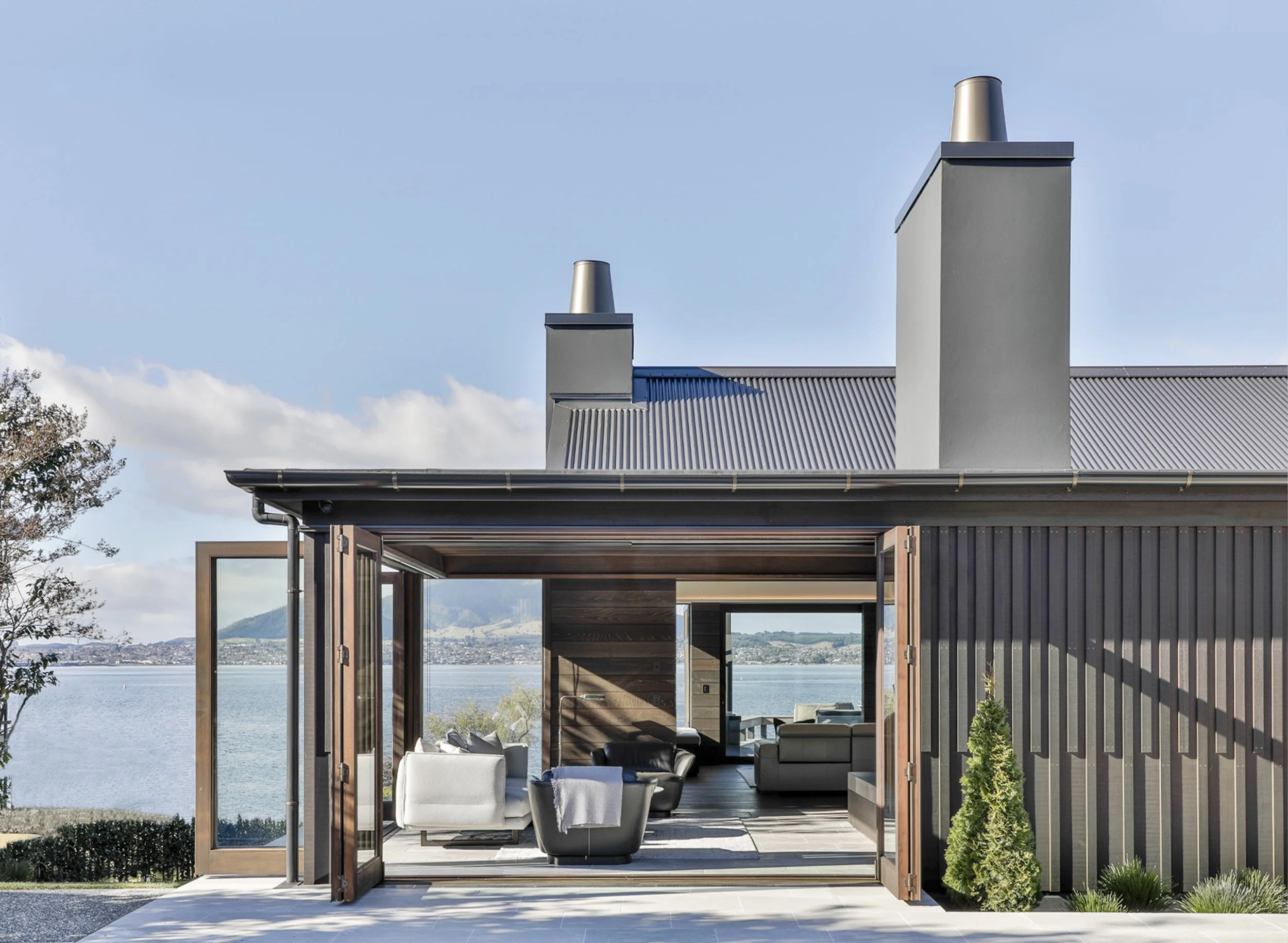 Modern house with large open glass doors, overlooking a Lake Taupo, with outdoor seating and a view of Mt Tauhara. Taupo Architect. Rotorua Architect. Lake Architect. New Zealand Architect. Hamilton Architect. Taranaki Architect. The Craftsmen Taupo 