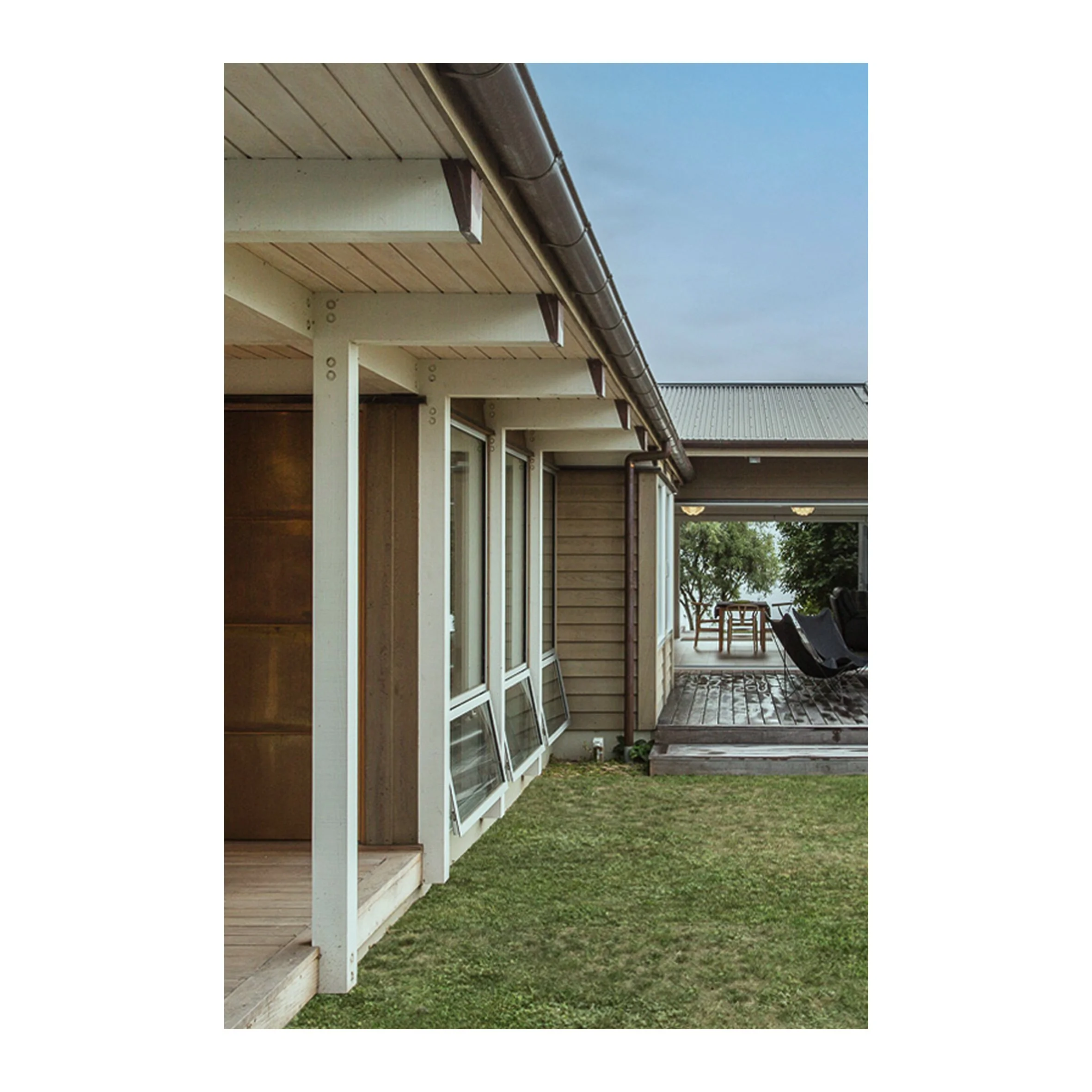 Exterior view of a house with a grassy yard, a deck, and sliding glass doors; windows leaning against the house, overcast sky.