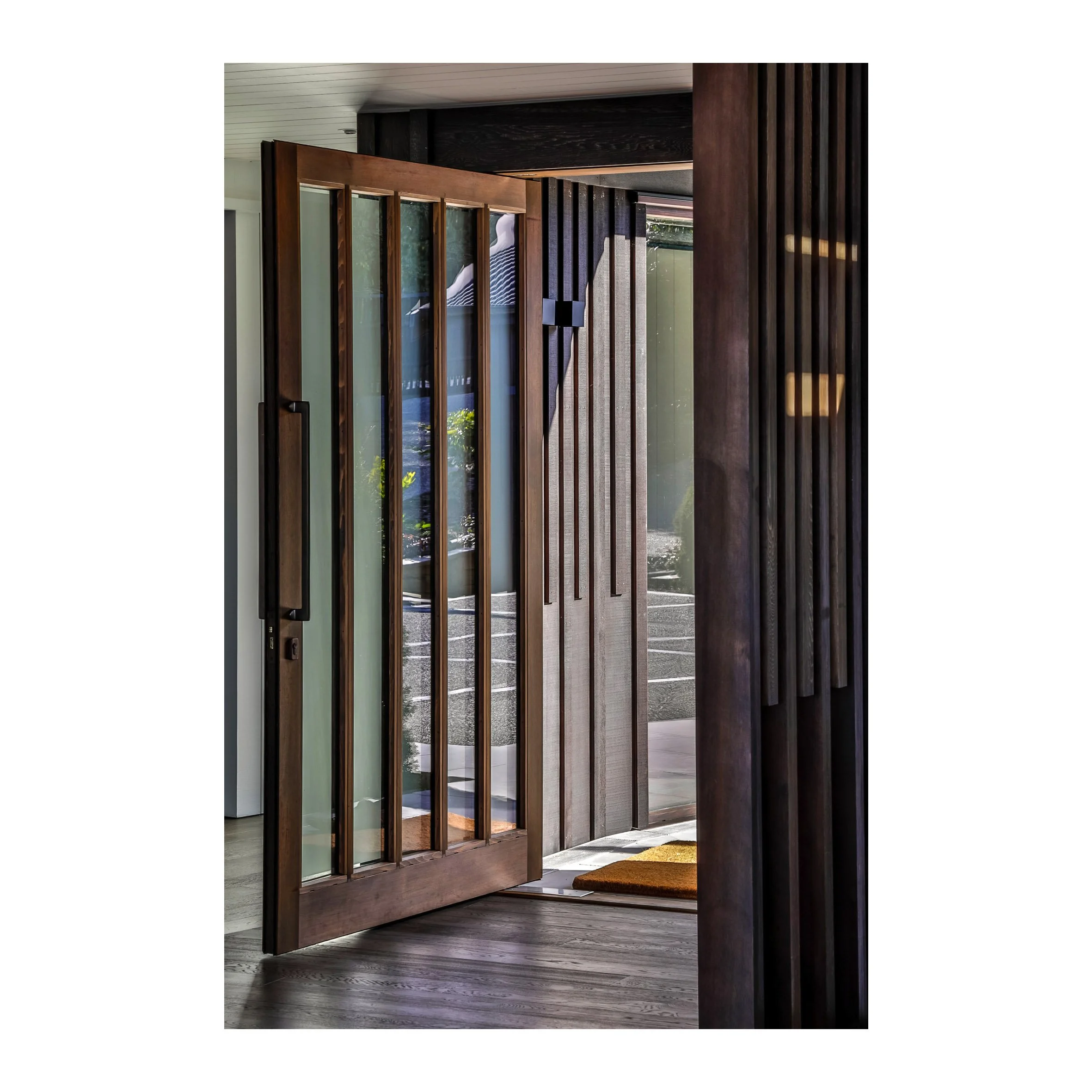 Open wooden front door with glass panels, revealing a patio or driveway outside.