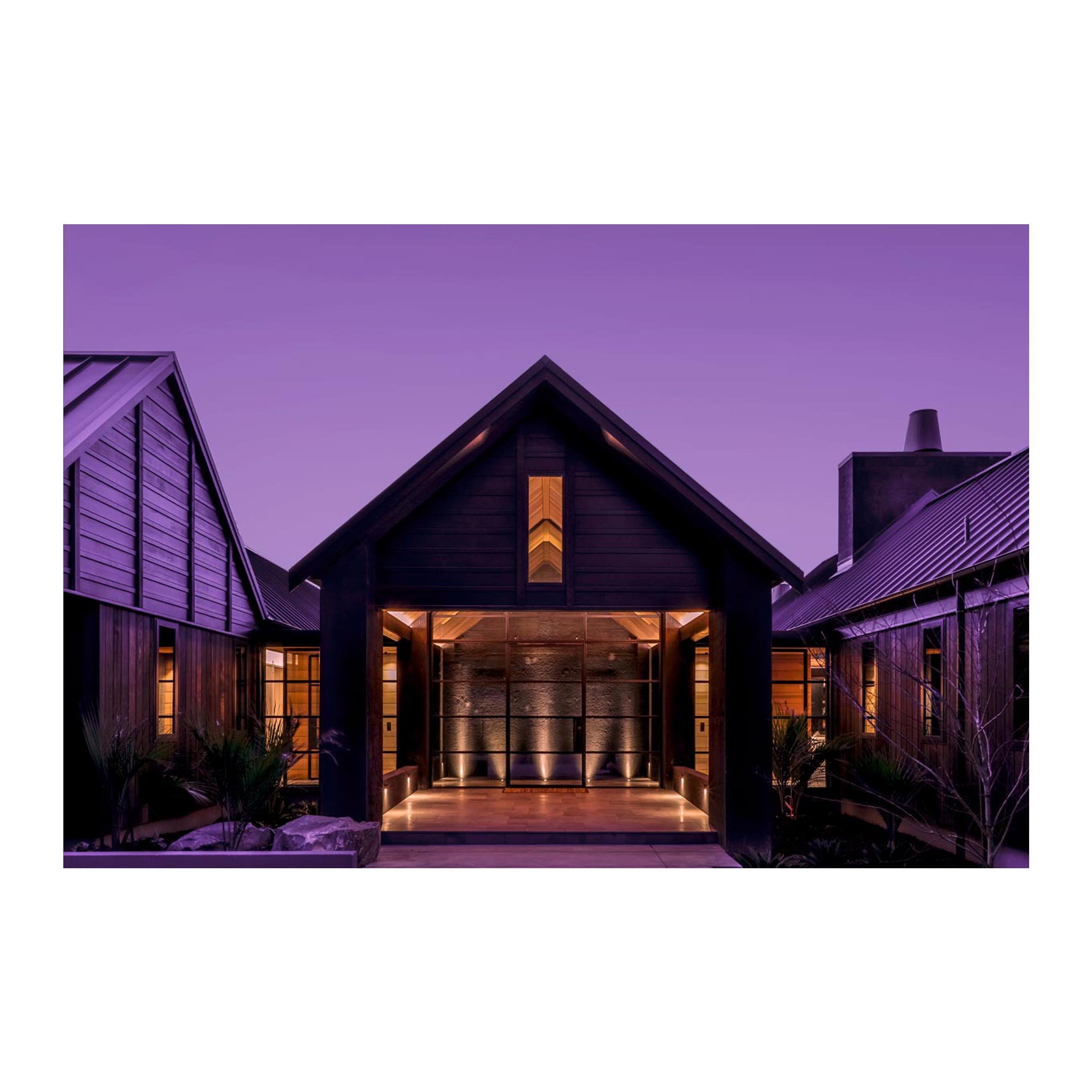 Modern building with dark wood exterior, illuminated entryway, and purple evening sky.
