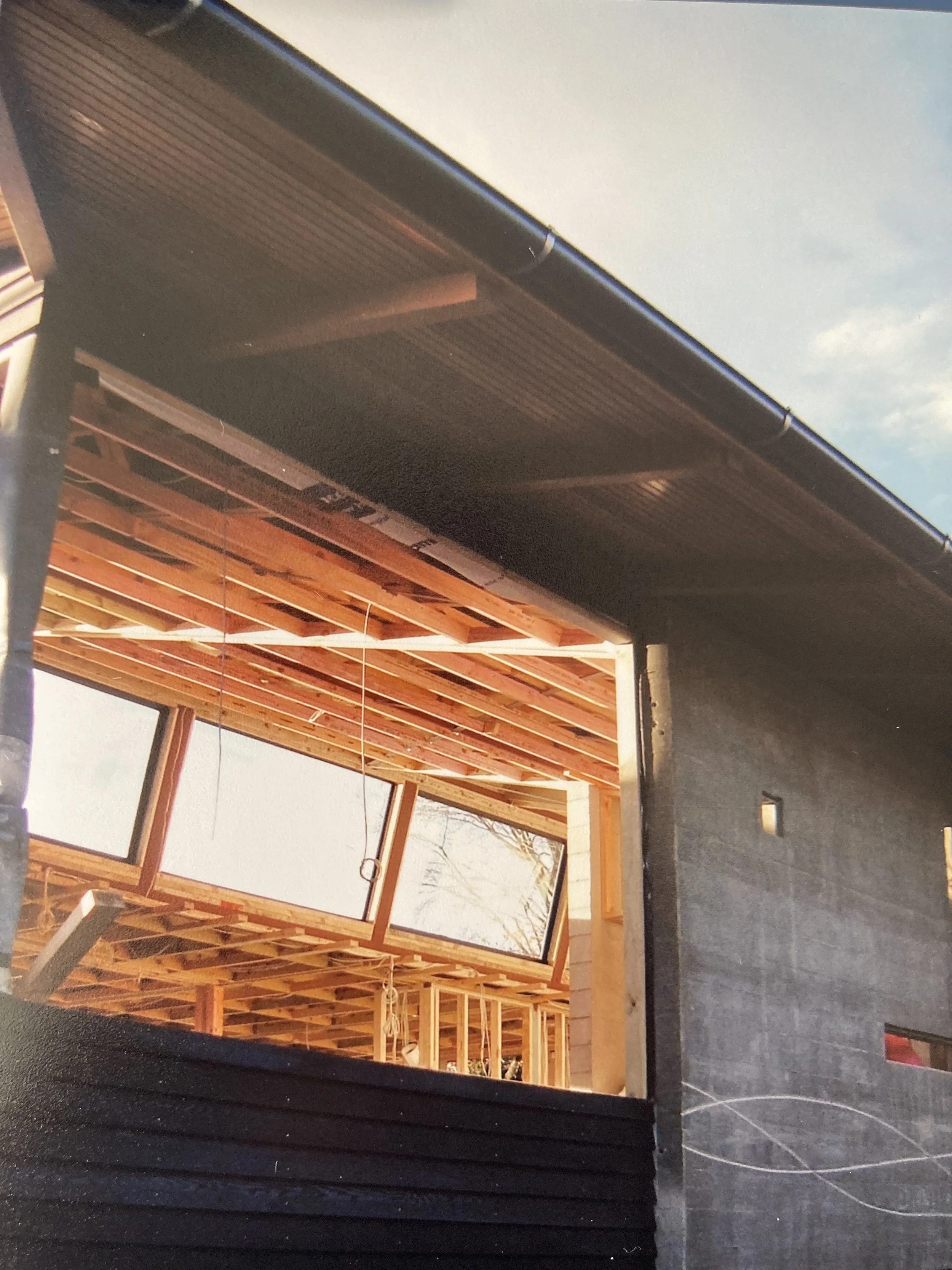 Construction site of a house with a partially built wooden frame and large window openings, viewed from outside.