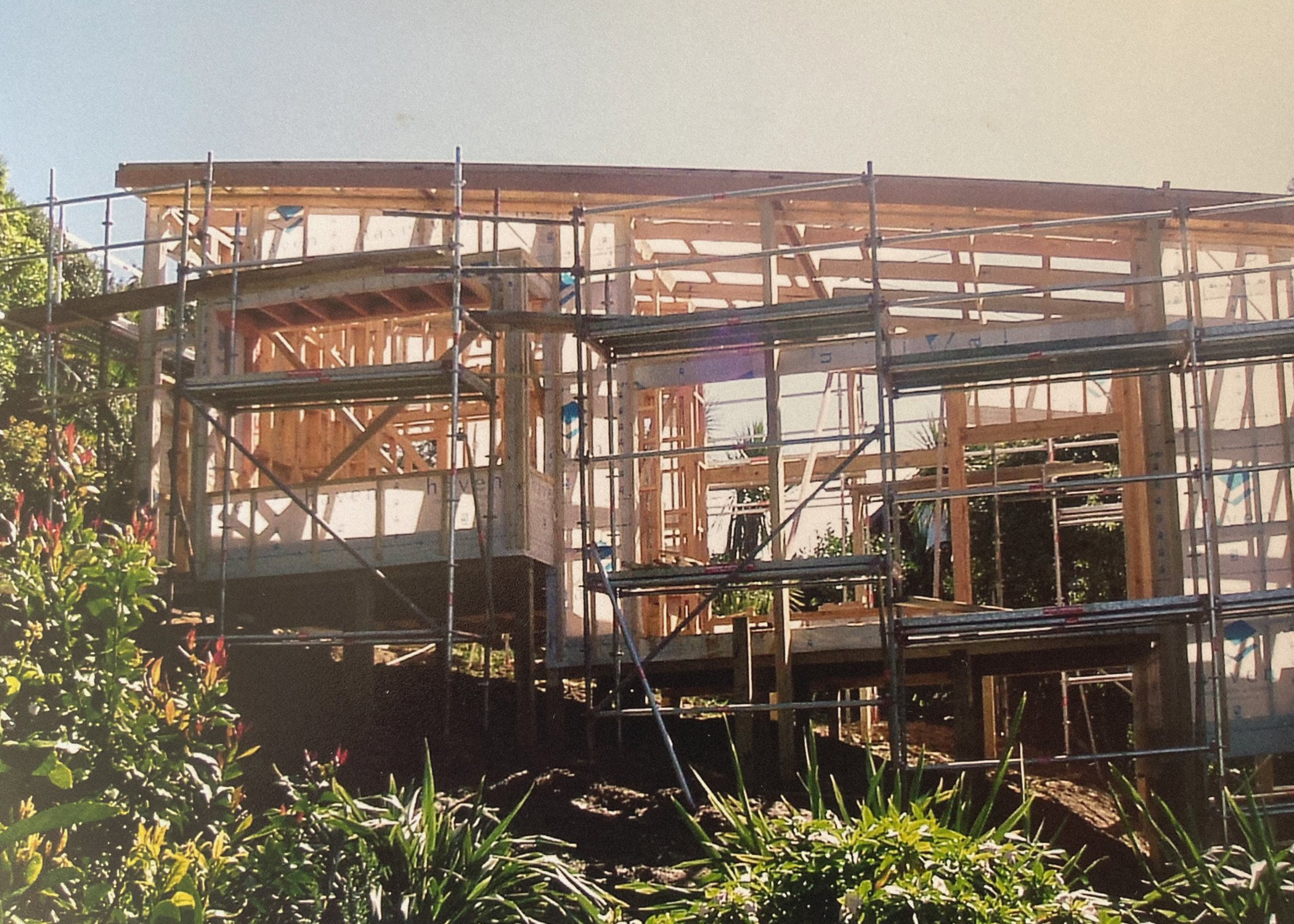 Wooden house under construction with scaffolding, surrounded by plants and trees. Bach Design New Zealand. Bach Architect. Holiday Home Architect. Rural Architect. 