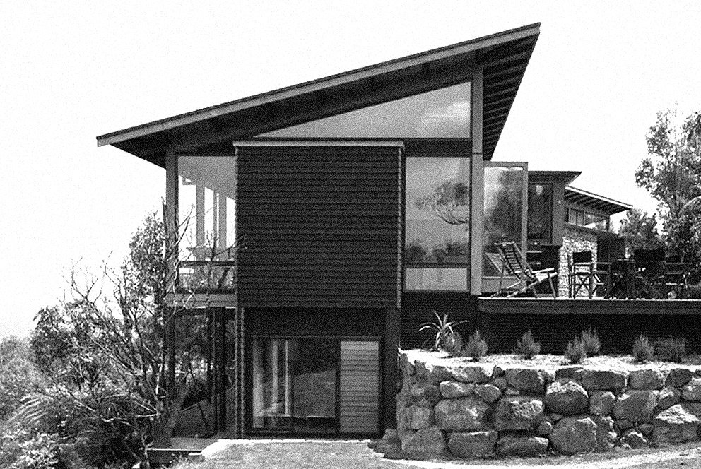 Modern house with a sloped roof, large glass windows, and stone landscaping.