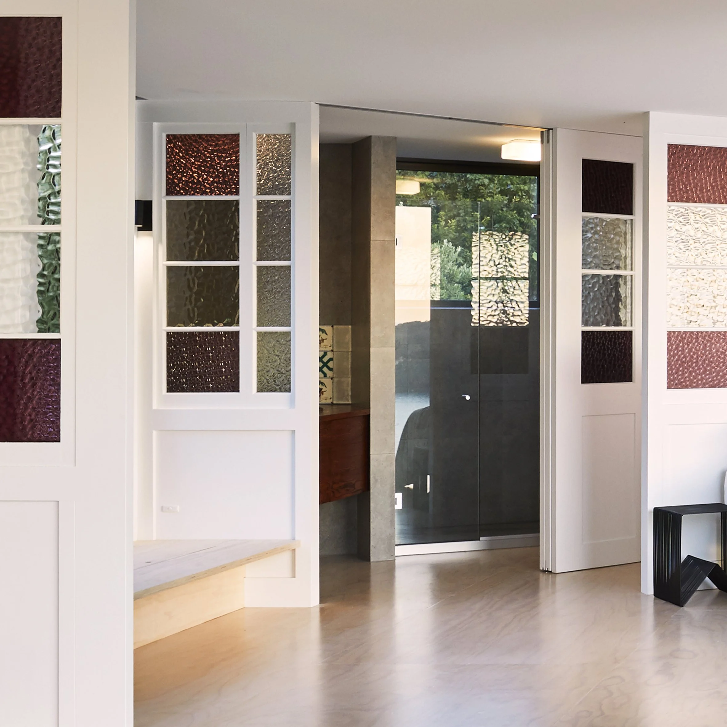 Interior view of a modern room featuring decorative divided glass panels, a frosted glass door, and a large window showing green trees outside.