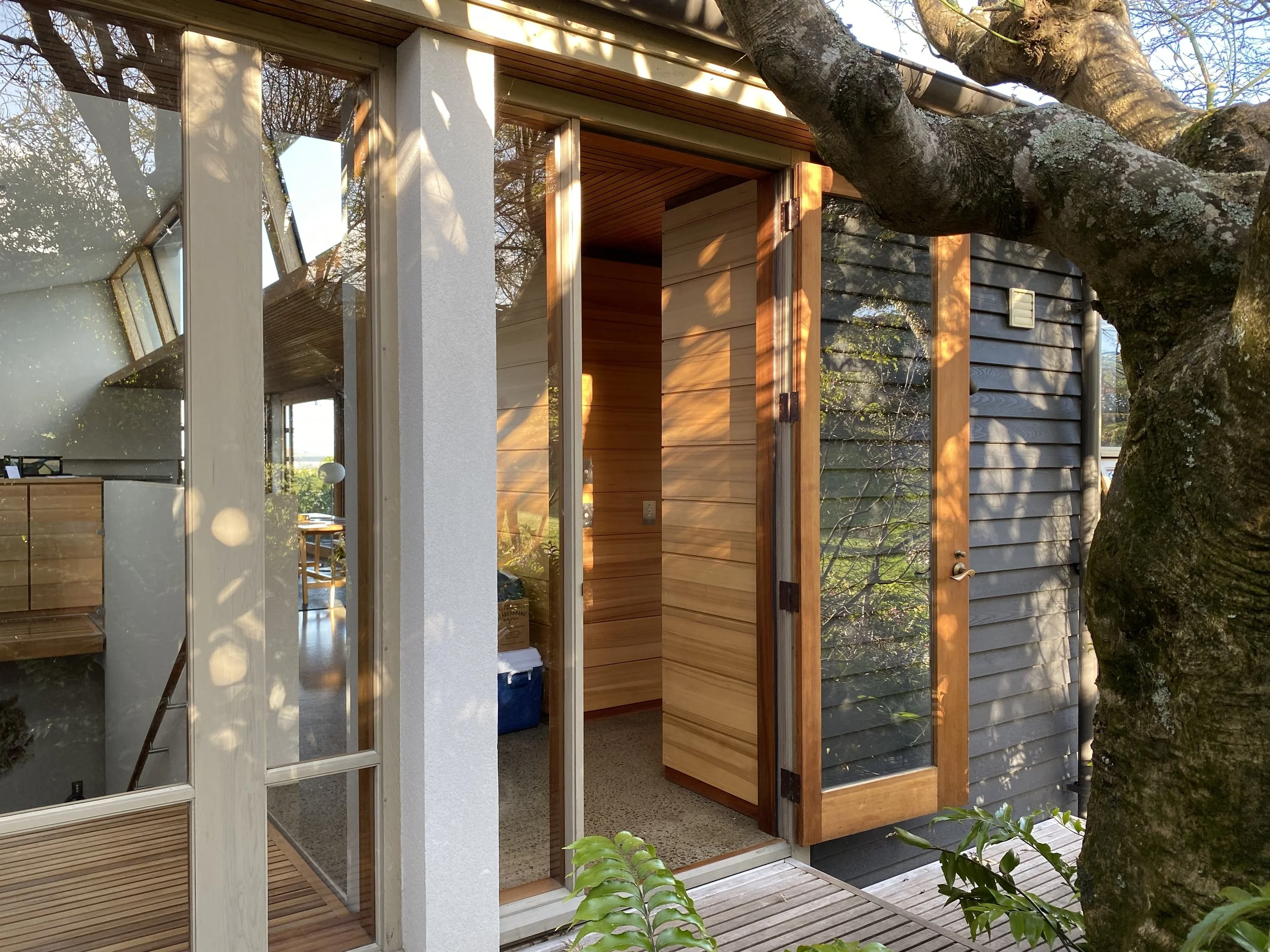 An exterior view of a modern house with glass and wood elements, including a door with a glass panel, surrounded by trees.