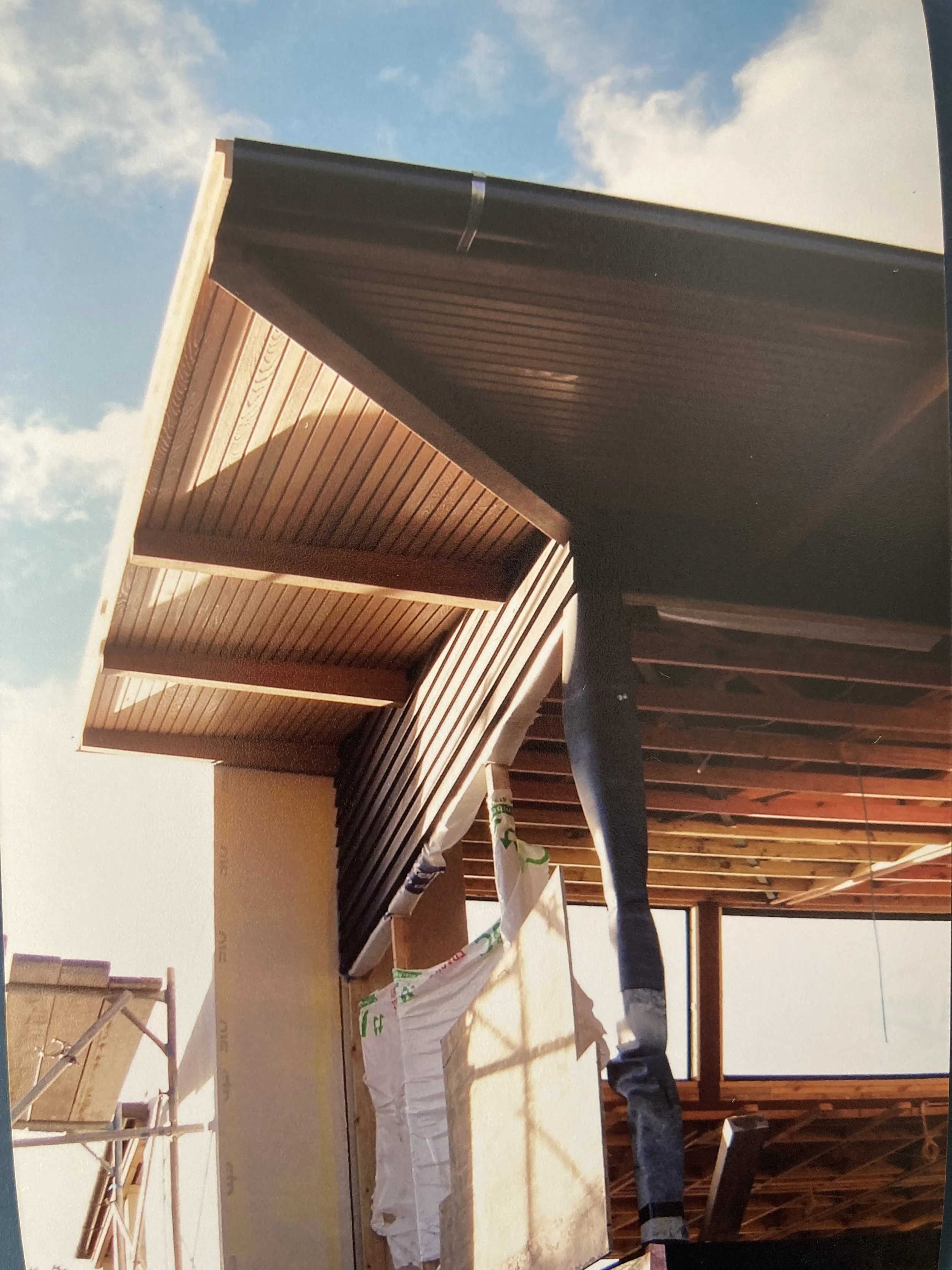Construction site with a building under construction, showing wooden framing and part of the exterior wall, with a blue sky background.