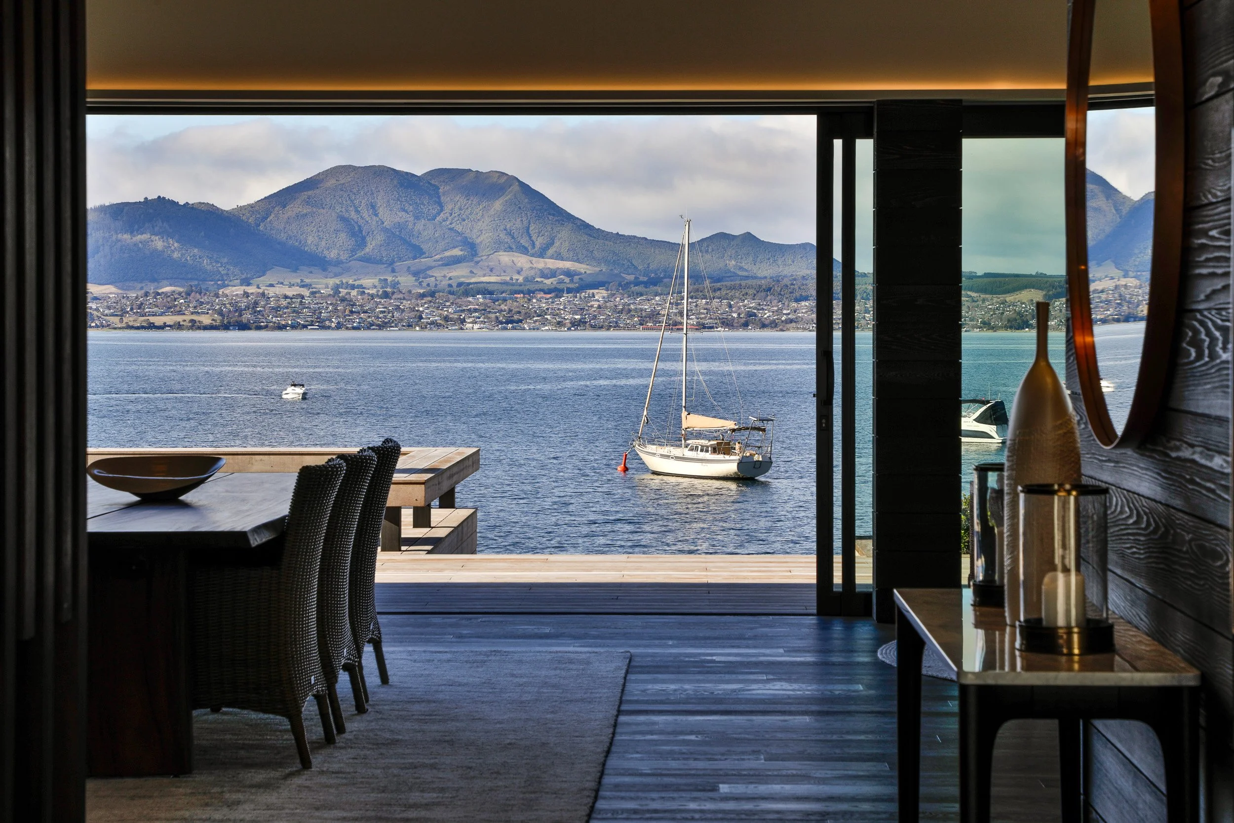 View from inside a house showing a deck with a sailboat on a river and mountains in the background. Taupo Architects. The Craftsmen Taupo Builders. 