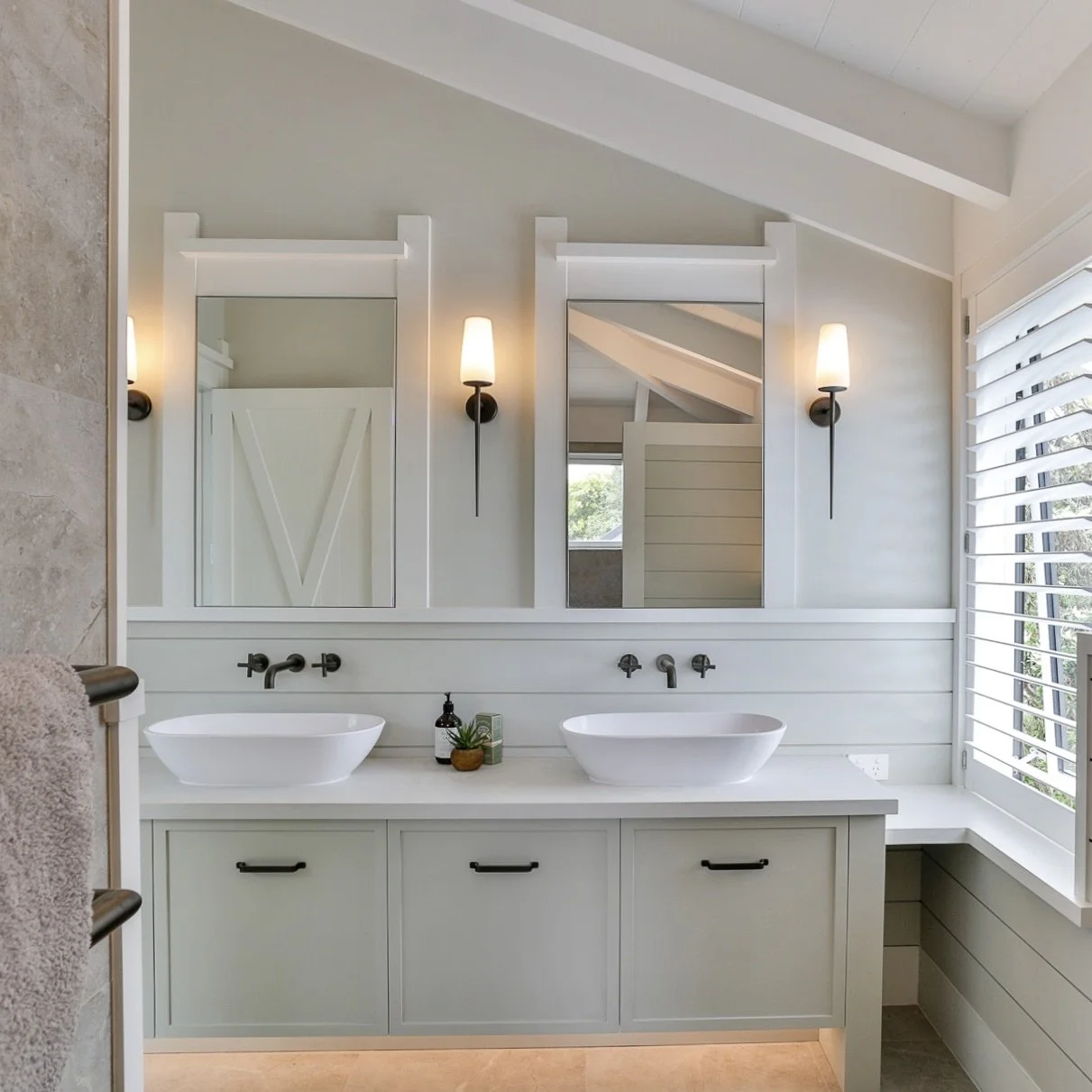 Modern bathroom with double white vessel sinks on a white vanity, two mirrors with white frames, two wall-mounted black sconces with white shades, a window with white shutters, and a beige tiled floor.