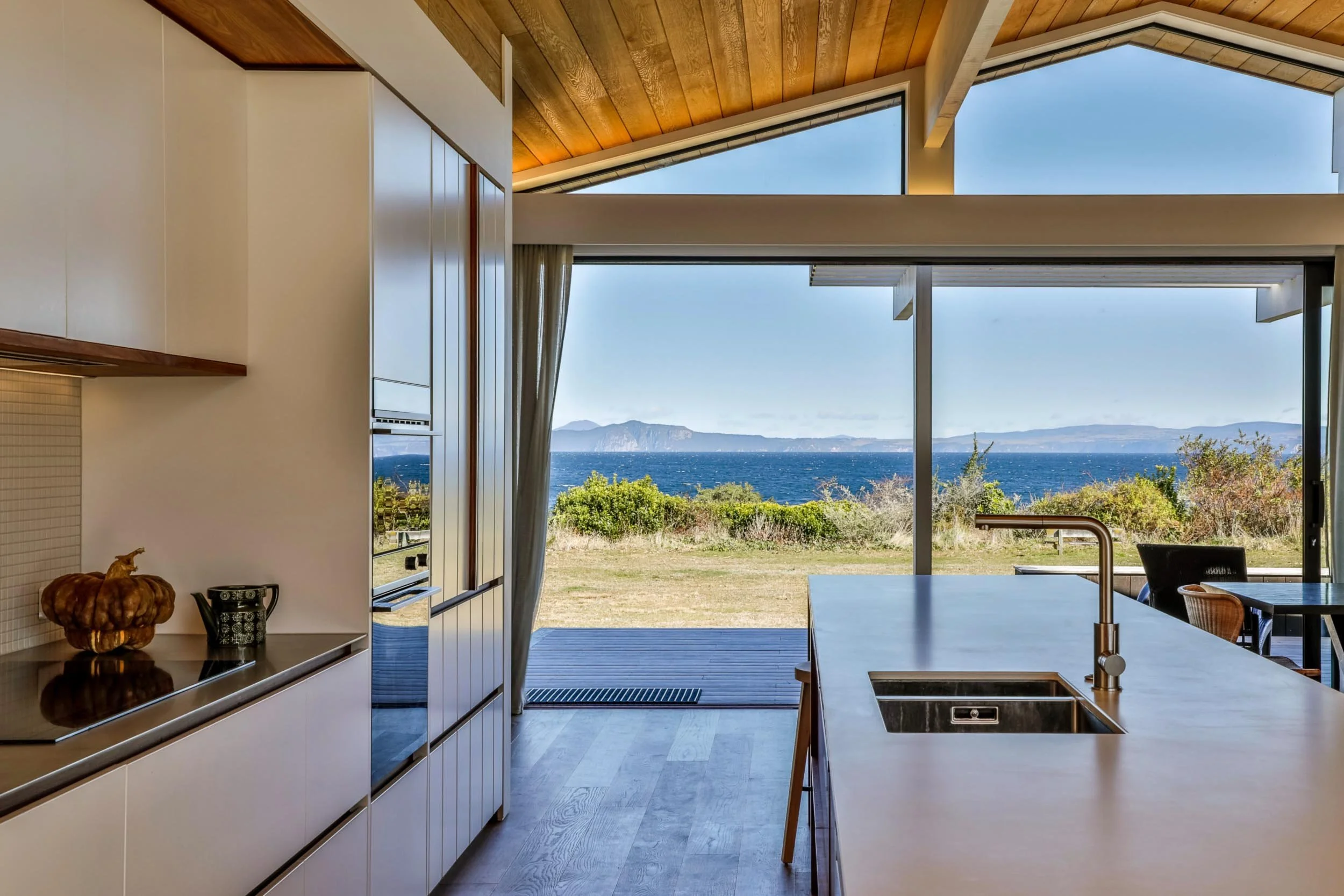 Interior view of a modern kitchen with an open window overlooking a field, ocean, and mountains in the distance.