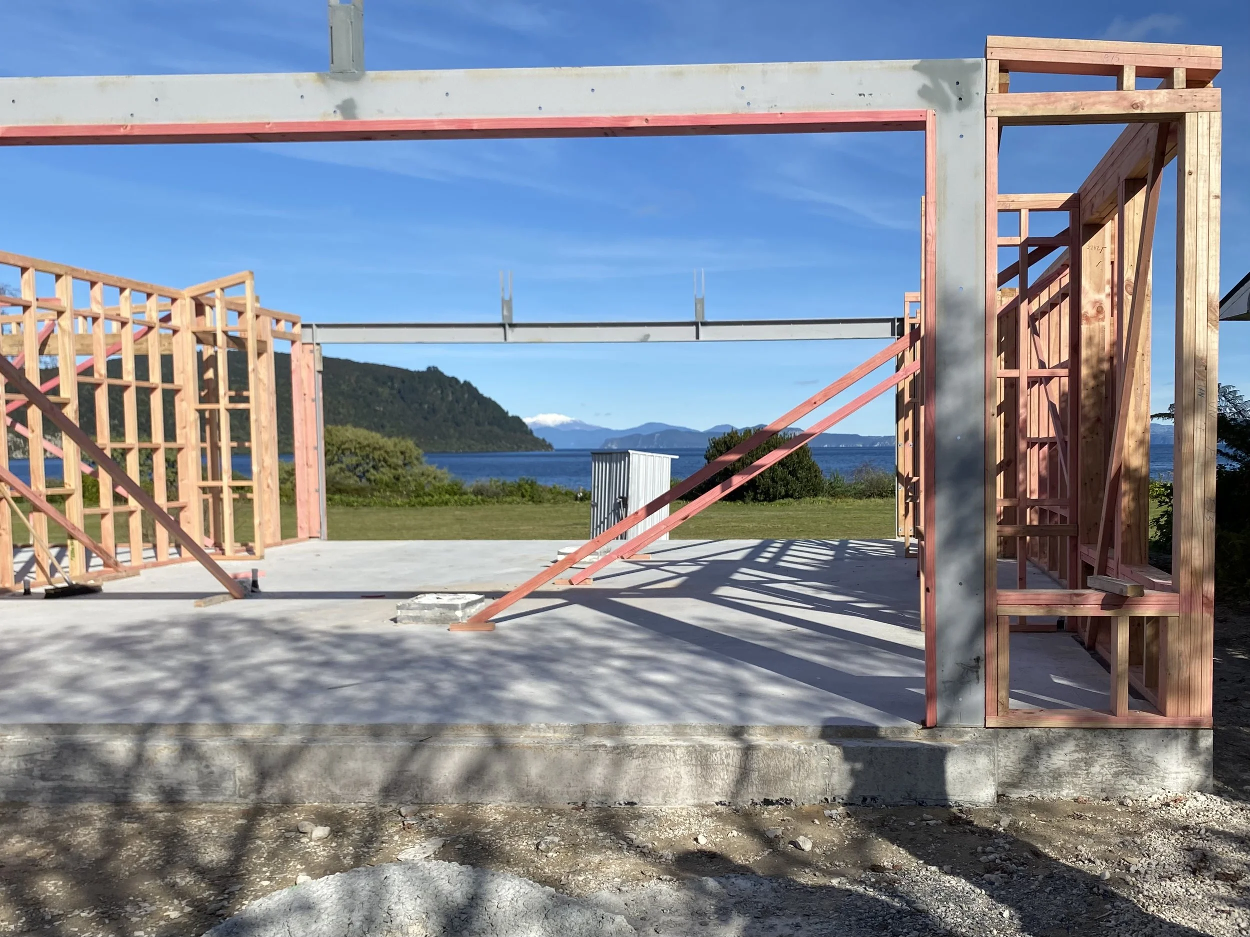 Construction of a building with wooden framing overlooking a body of water and mountains in the background.