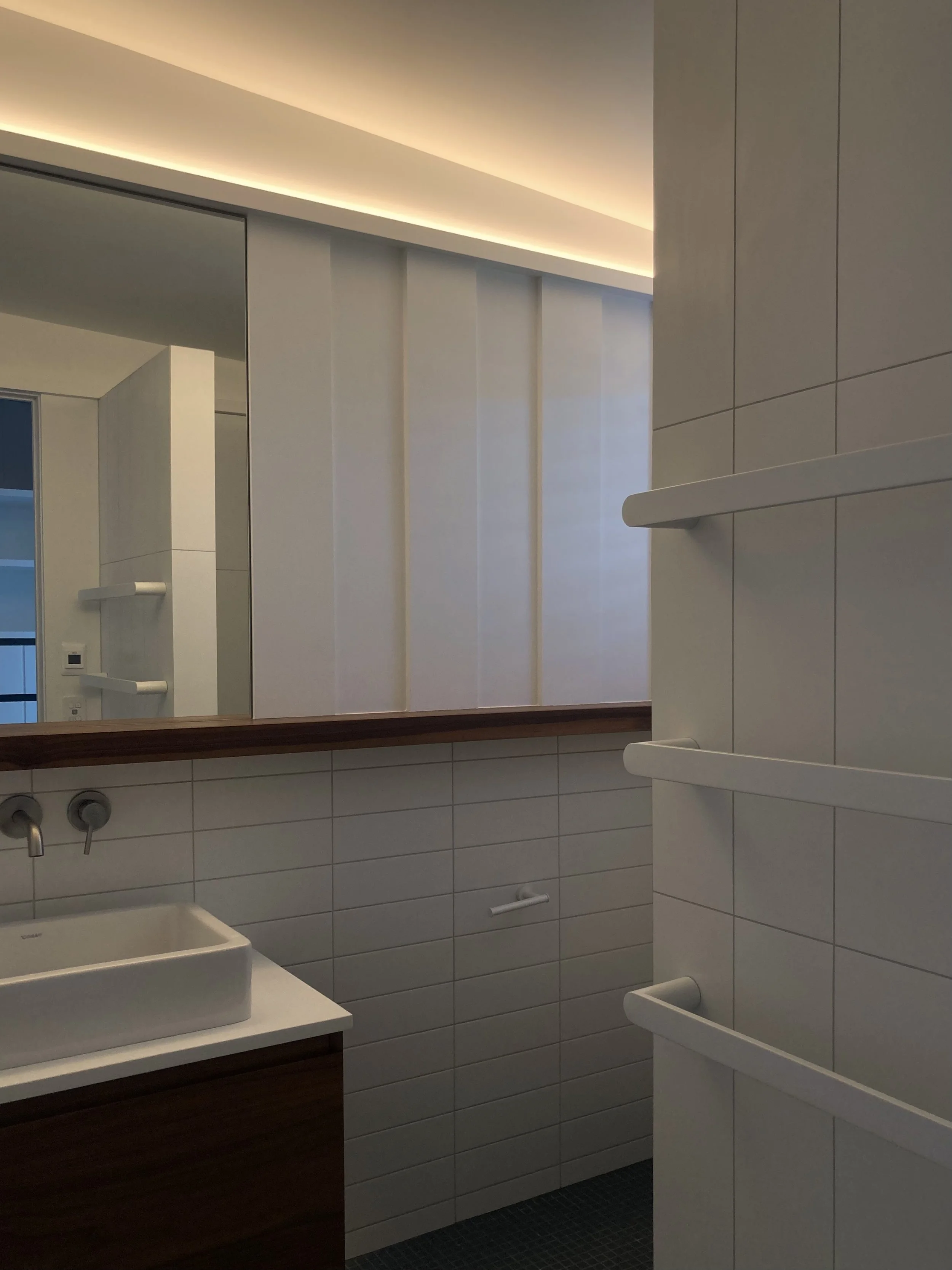 Modern bathroom with white tiles, a rectangular sink, a dark wood vanity, a large mirror, and white wall-mounted shelves.