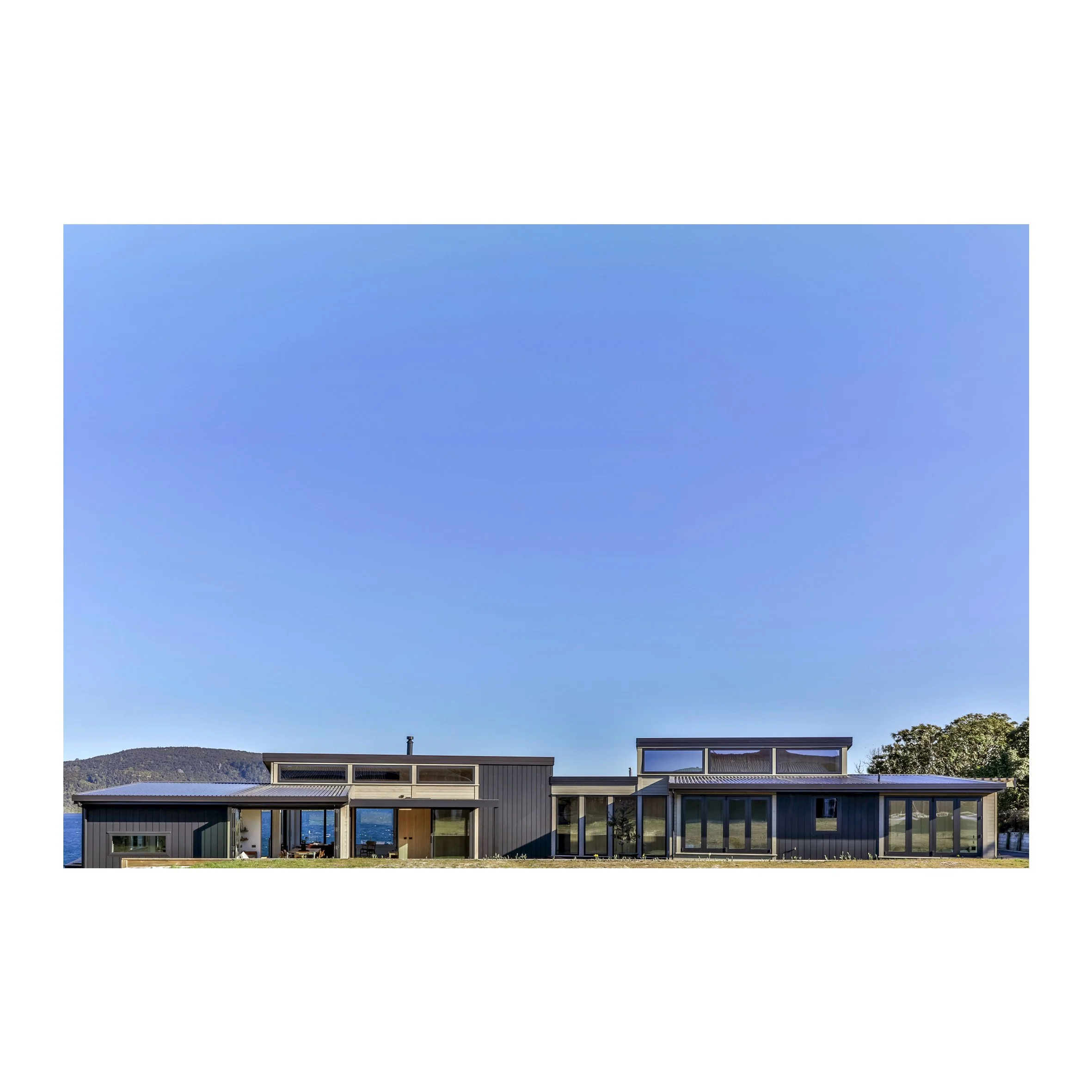 Modern house with gray exterior, large glass windows, and multiple levels, set against a clear blue sky and distant hills.