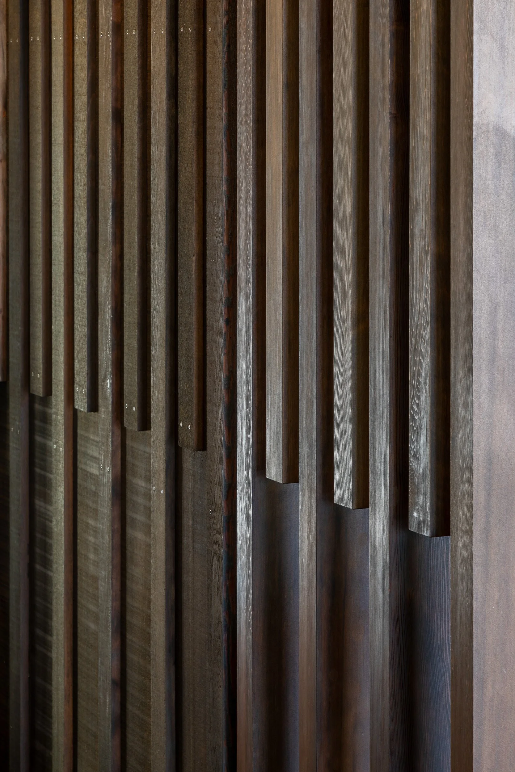 Close-up of a wall with vertical wooden slats of varying widths and shades. Taupo Architects. The Craftsmen Taupo Builders. Architectural Builders Taupo. 