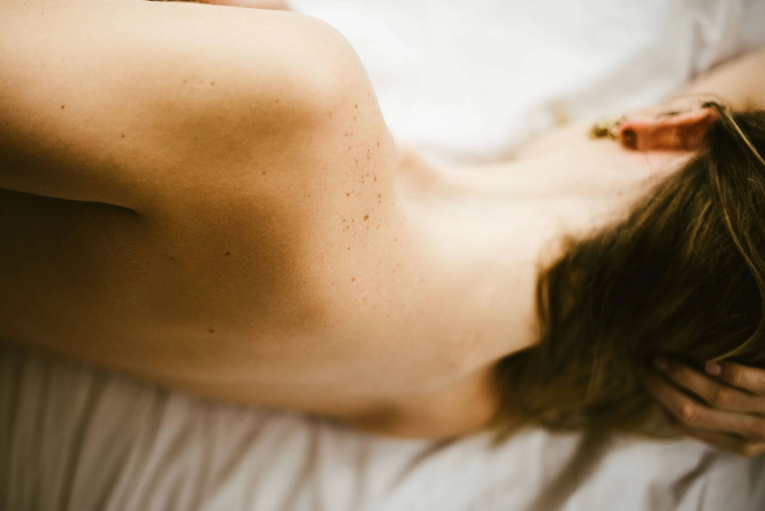 Close-up of a person's shoulder, neck, and part of the face with freckles, with brown hair visible.
