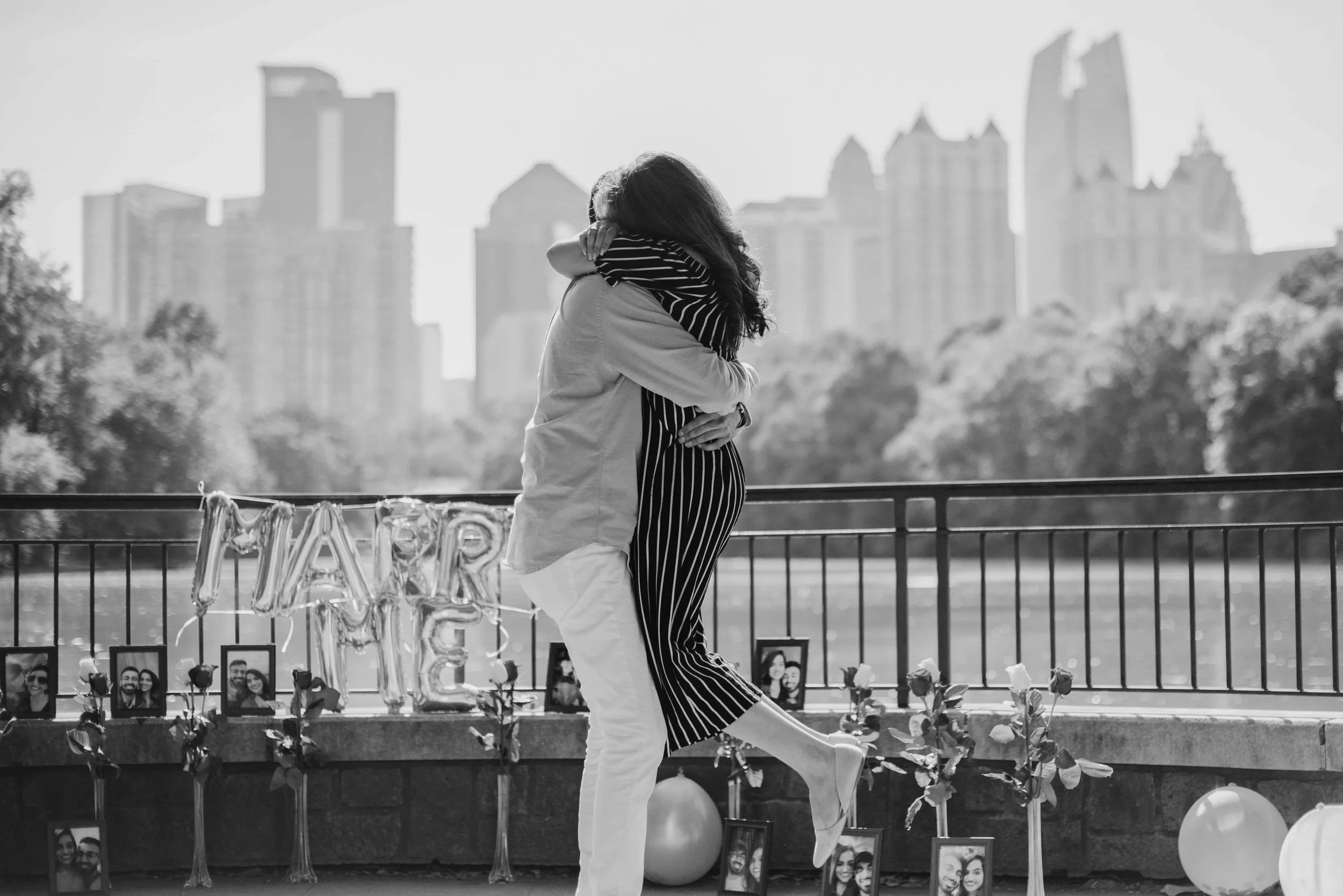 A woman and a girl embracing at a memorial decorated with photos and balloons in an urban park.