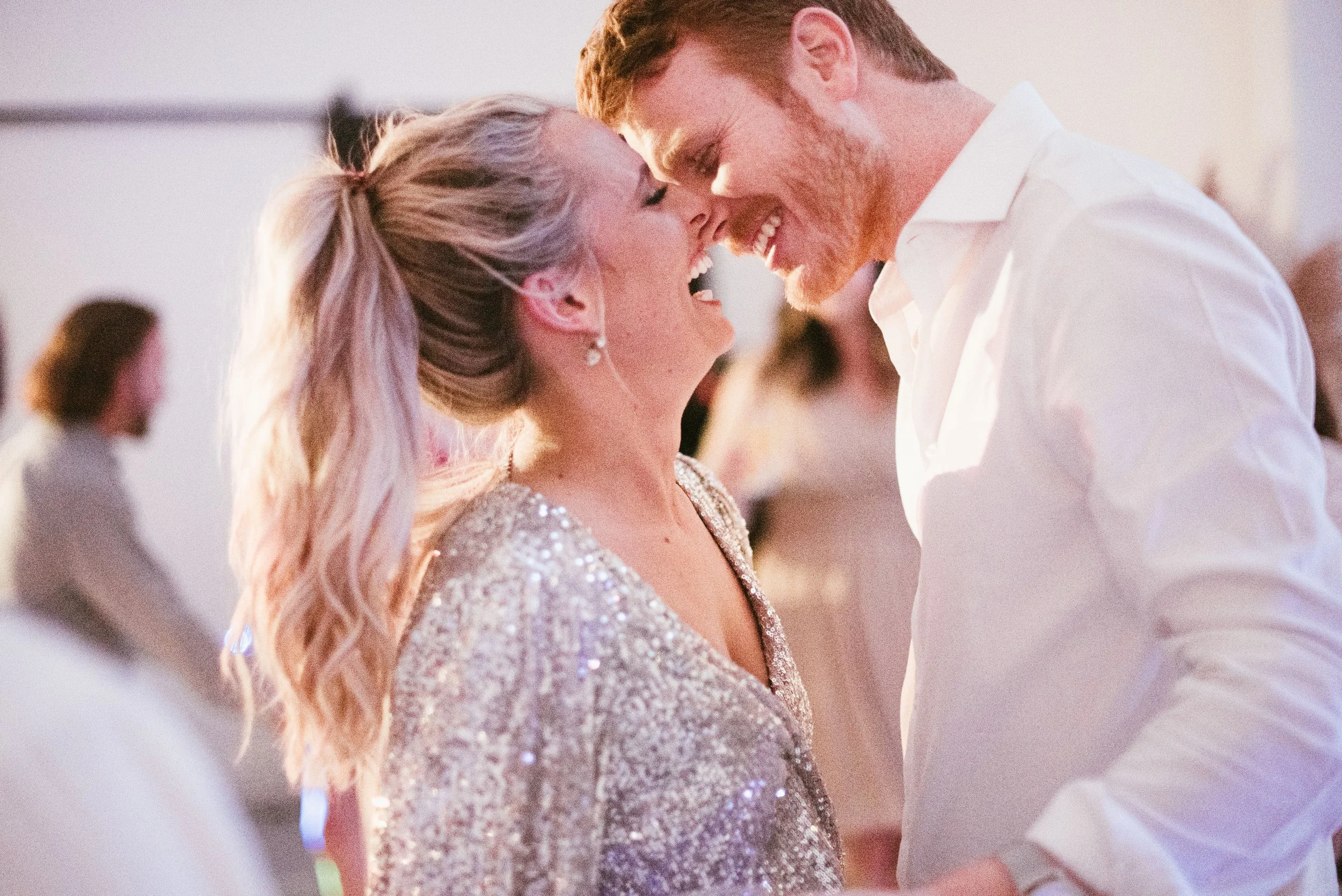 A smiling woman and man with their foreheads touching, enjoying a close moment together at a celebration.