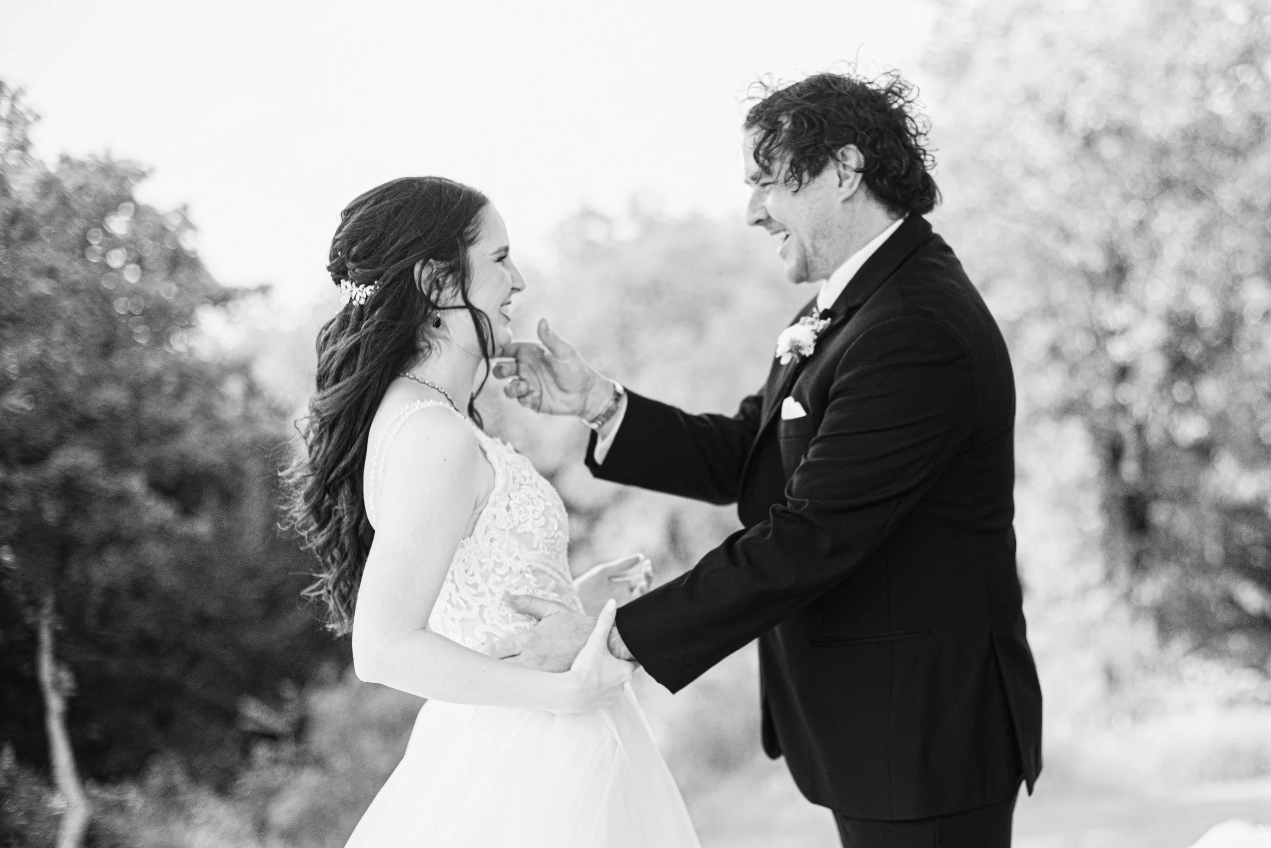 A bride and groom share a joyful moment outdoors during their wedding, smiling and holding hands.