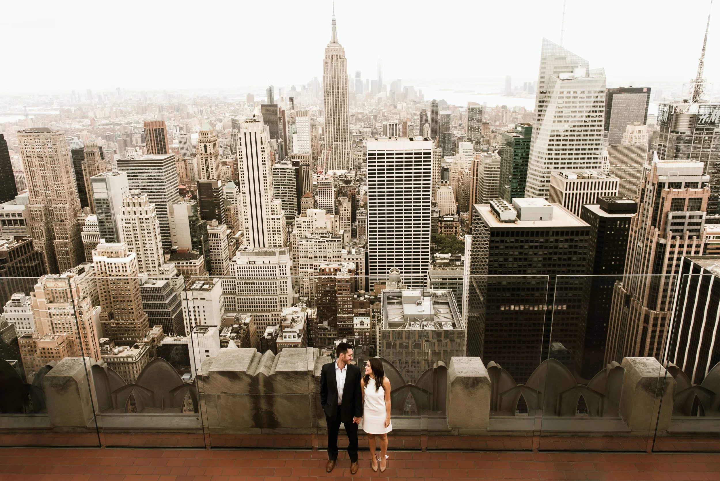 A man and woman standing on a rooftop with the New York City skyline in the background.