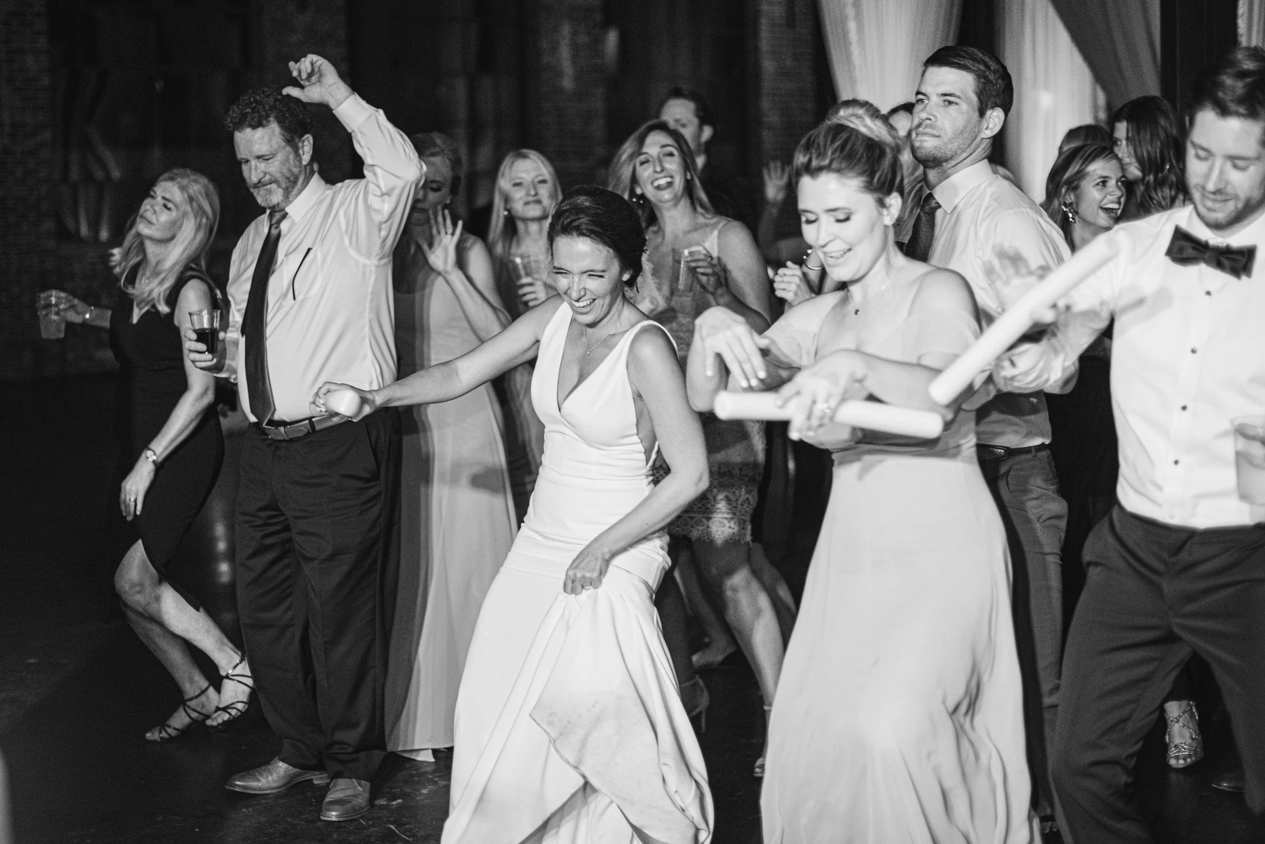 A group of people, dressed formally, dancing and celebrating at an event or party, with smiles and laughter visible on their faces.
