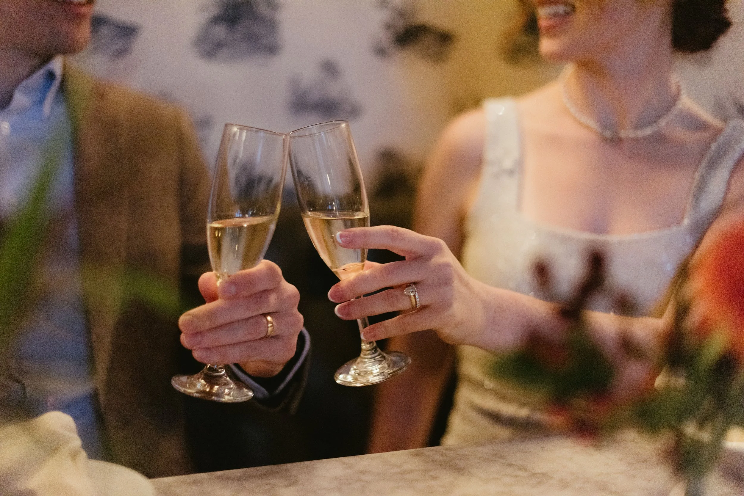 Two people dressed elegantly, a man and a woman, raising champagne glasses in a toast at a celebration or wedding reception.