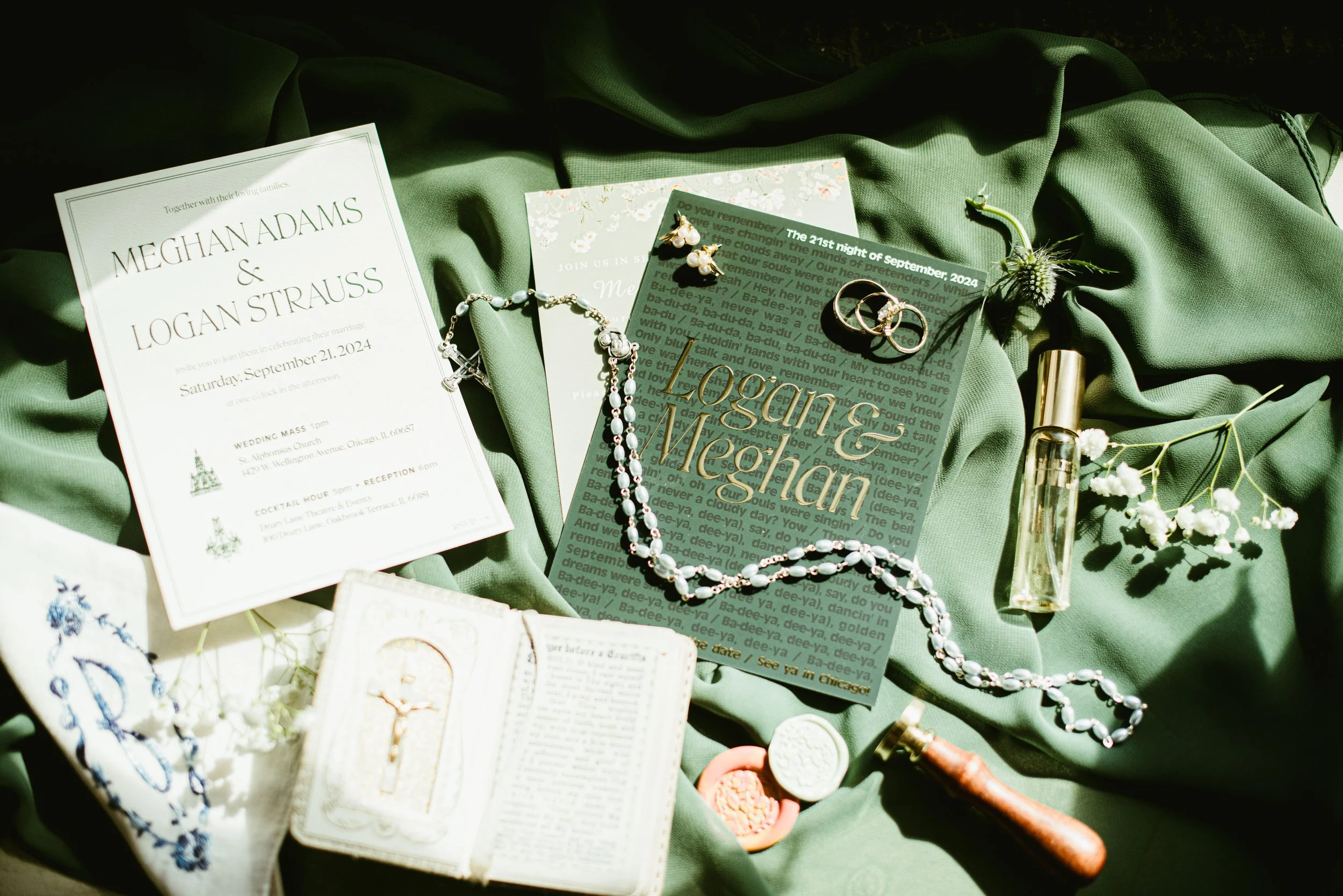 Wedding invitation, jewelry, and vintage items laid out on a green fabric surface for a wedding celebration.