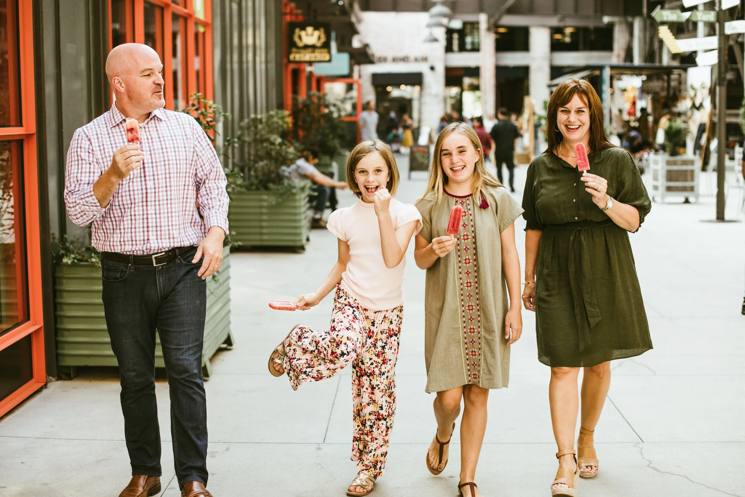 A group of four people enjoying ice cream cones while walking outside on a city street. They are smiling and appear to be happy.