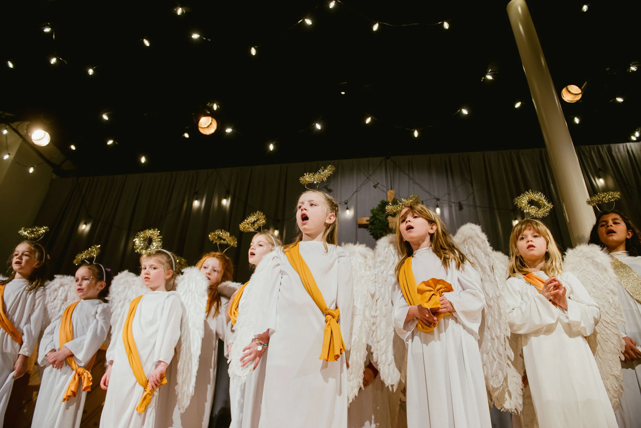 Children dressed as angels singing on stage with Christmas decorations.