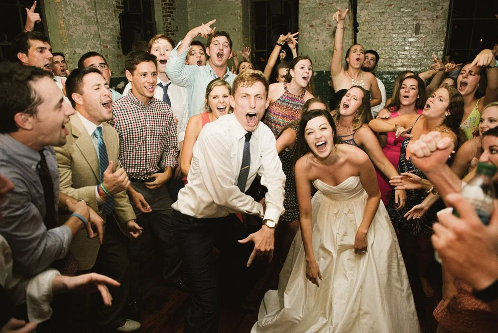 People dancing and having fun at a celebration or wedding reception, with joyful expressions and energetic gestures.