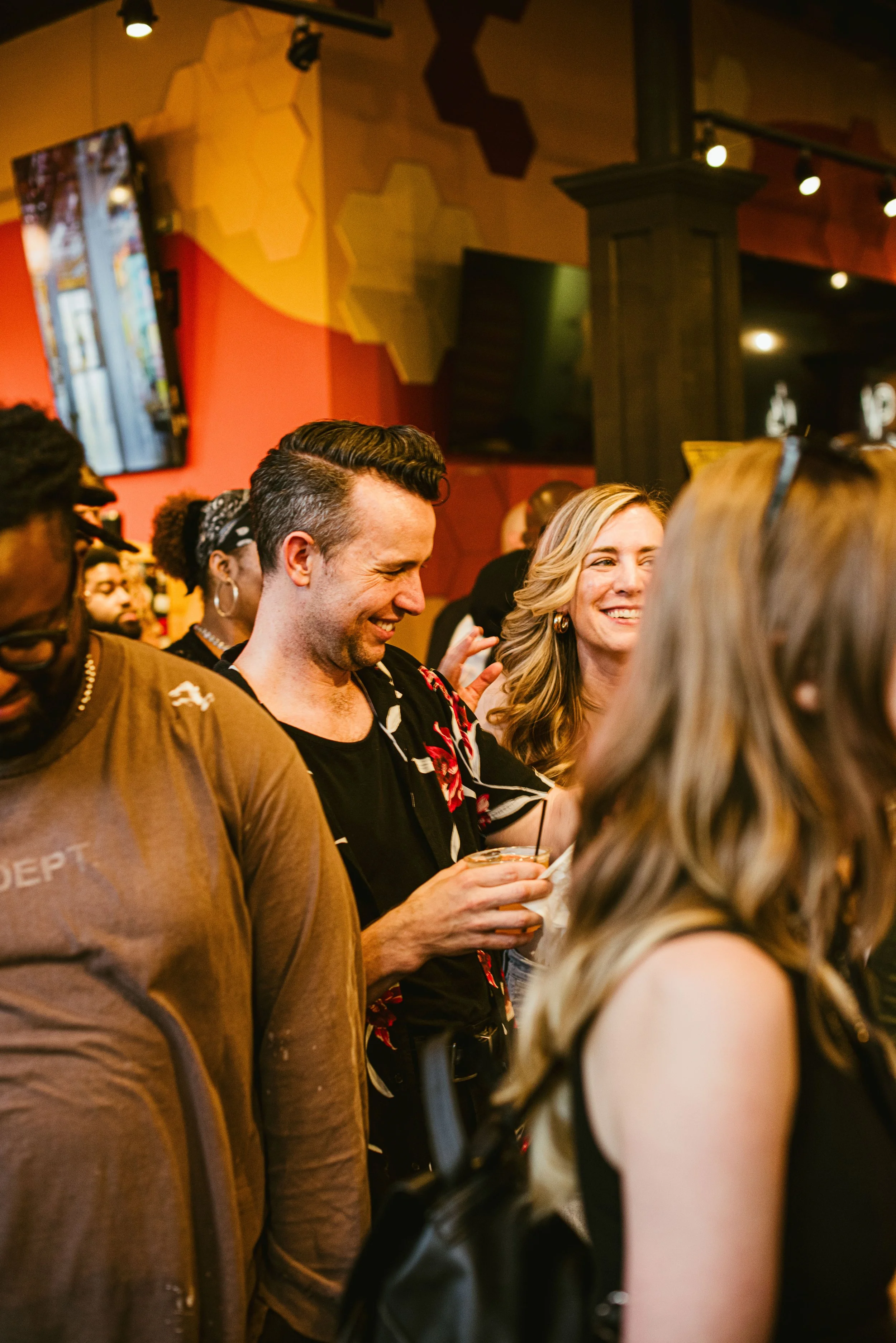 People socializing in a bar or restaurant, smiling and holding drinks.
