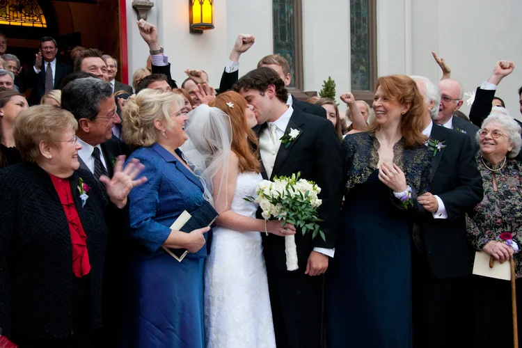 Bride and groom kissing surrounded by wedding guests celebrating indoors.