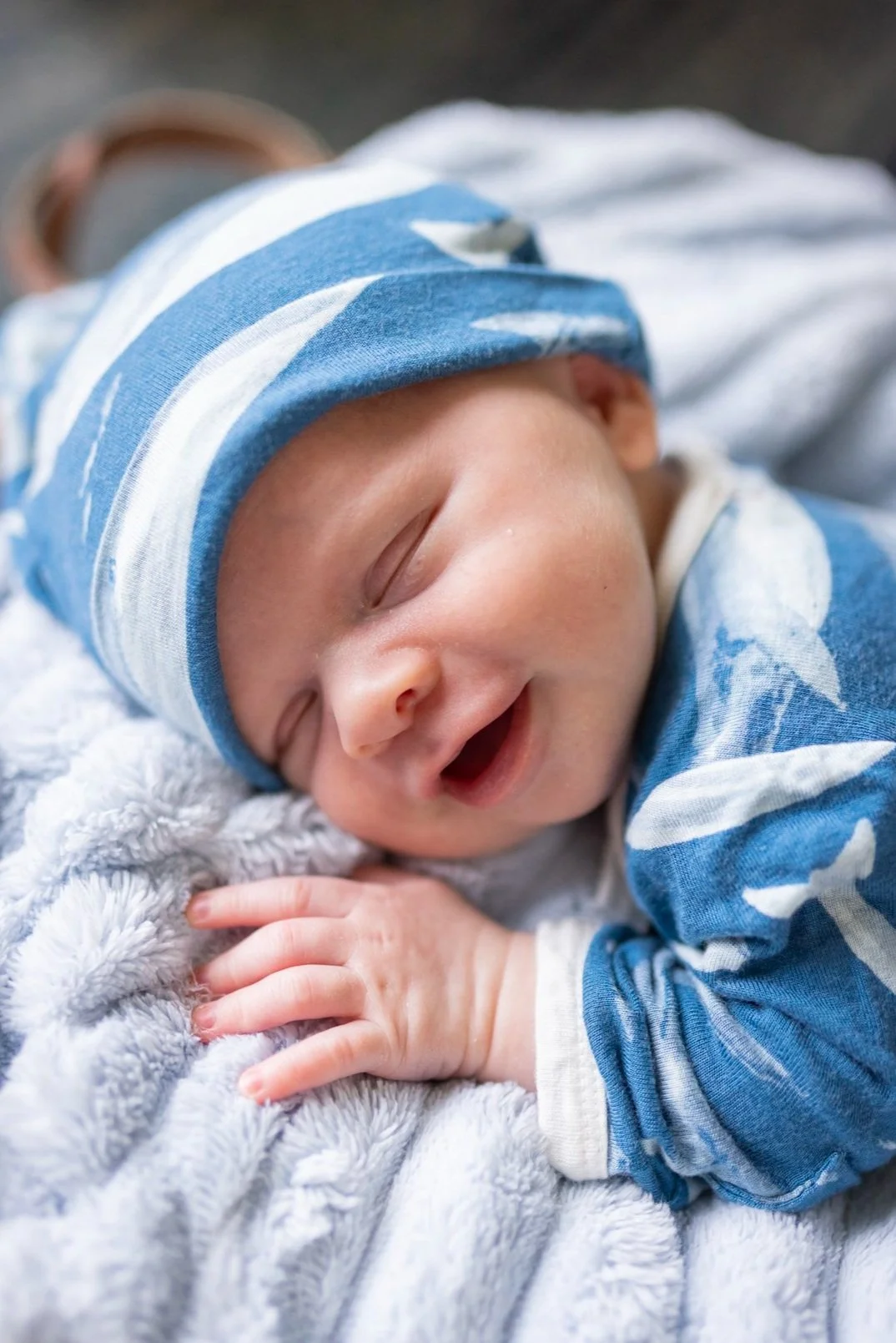 Close-up of a sleeping baby wearing a blue and white striped hat and a matching blue outfit, lying on a soft gray blanket.