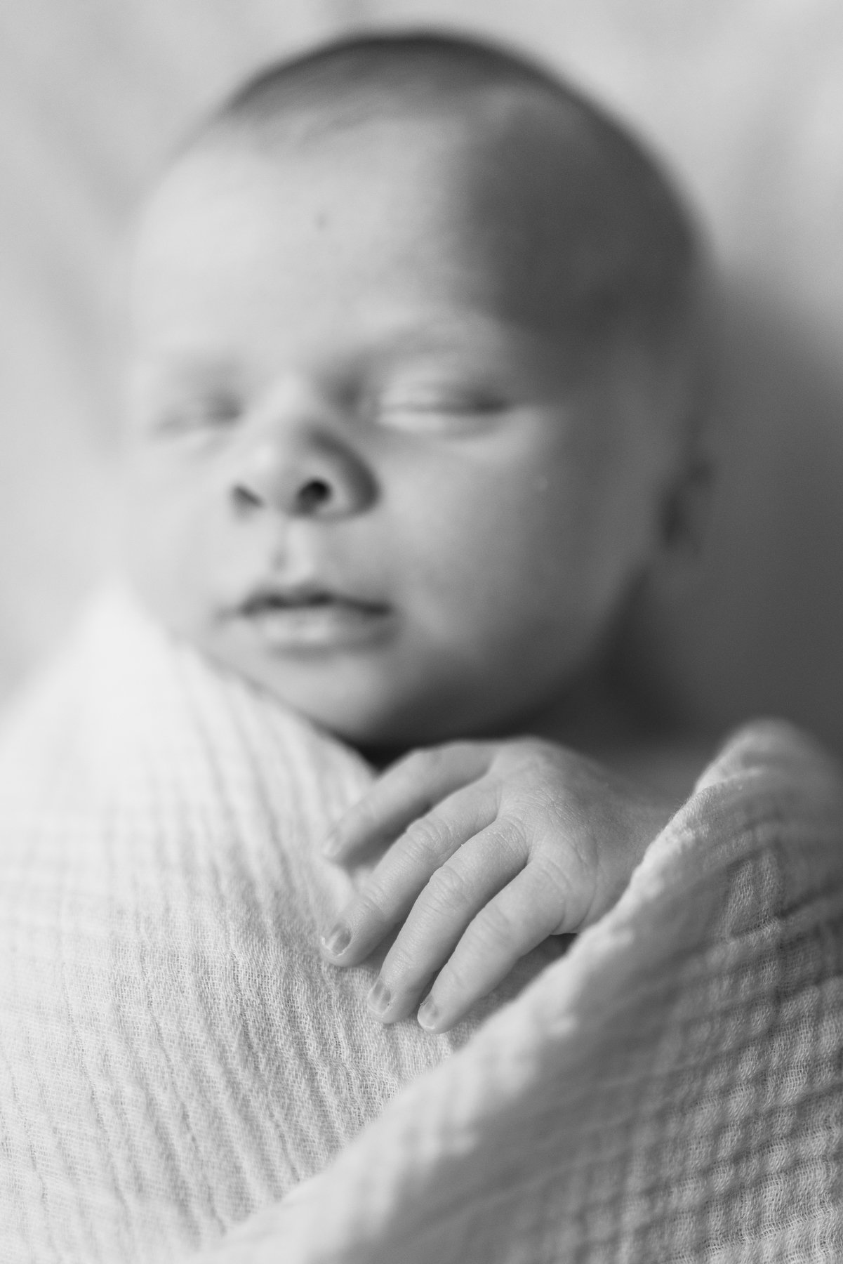 Black and white close-up of a baby's face and hand, sleeping peacefully.