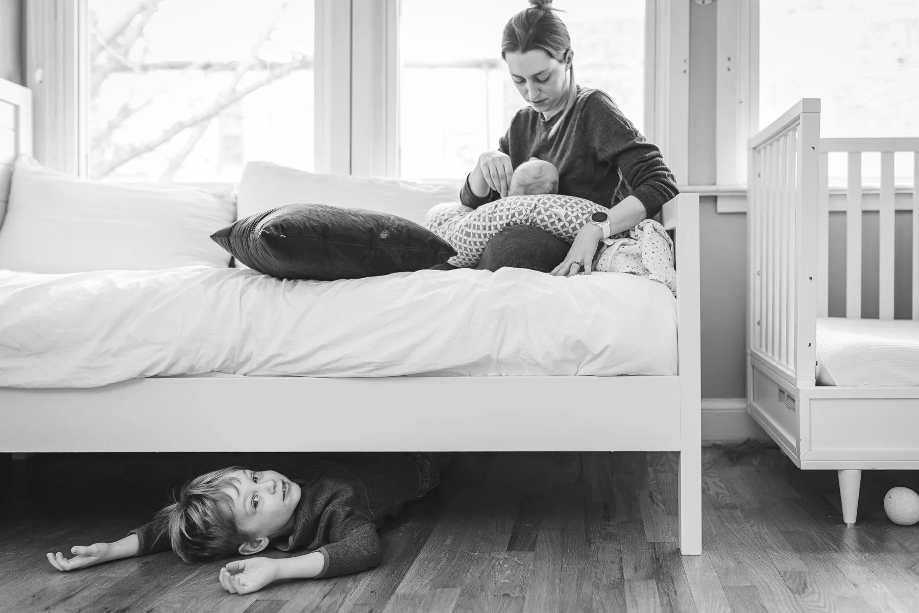 Newborn lifestyle portrait on a bed with mom and older sibling hiding underneath.