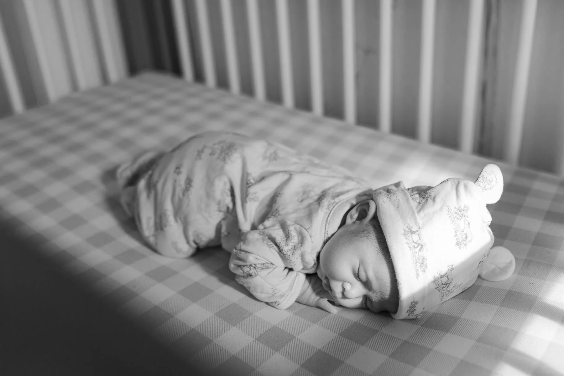 A baby sleeping on a bed, wearing a hoodie with bear ears, in a room with unfinished walls.