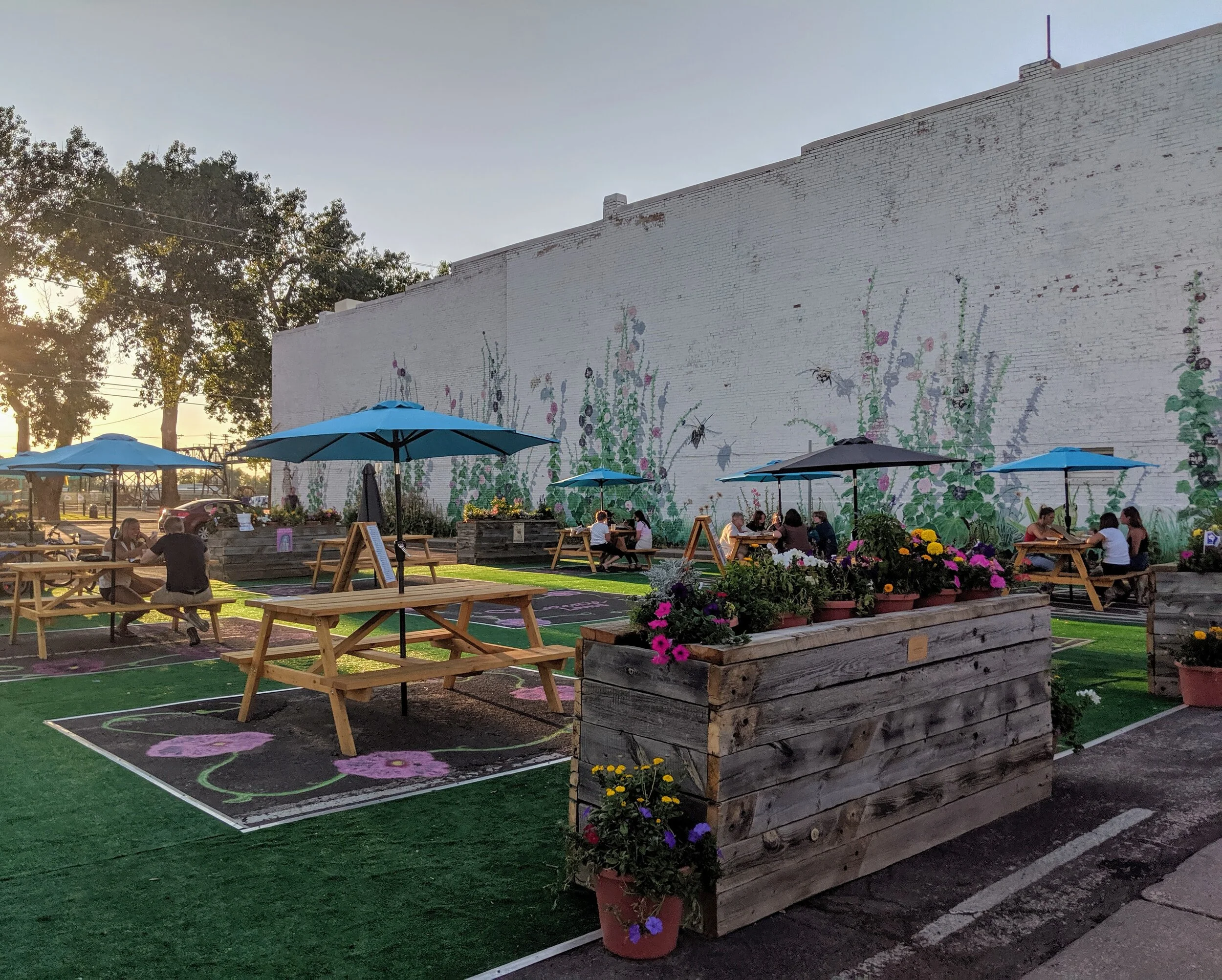 People sitting at picnic tables with a mural of hollyhocks behind them