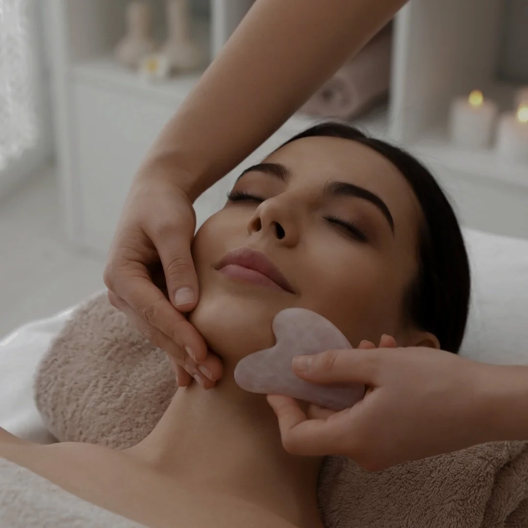 Femme recevant un massage au visage avec un galet en pierre rose dans un spa.