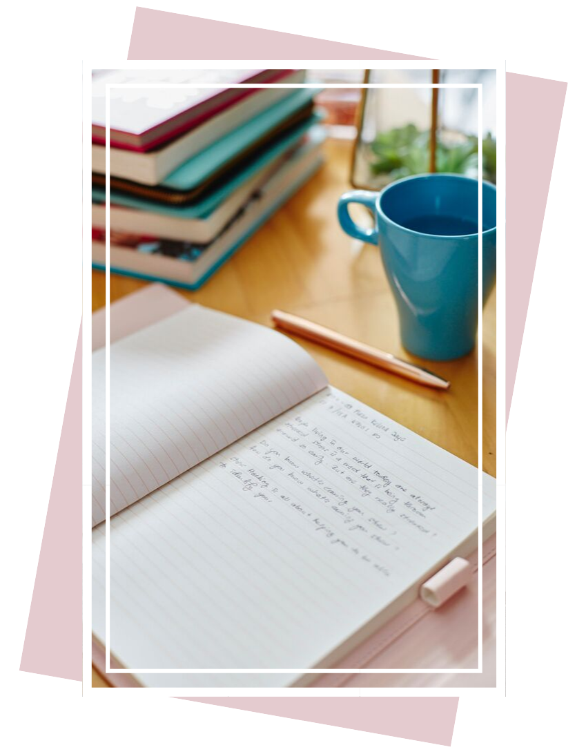 An open journal on a table with a teal coffee mug and stack of books in the background