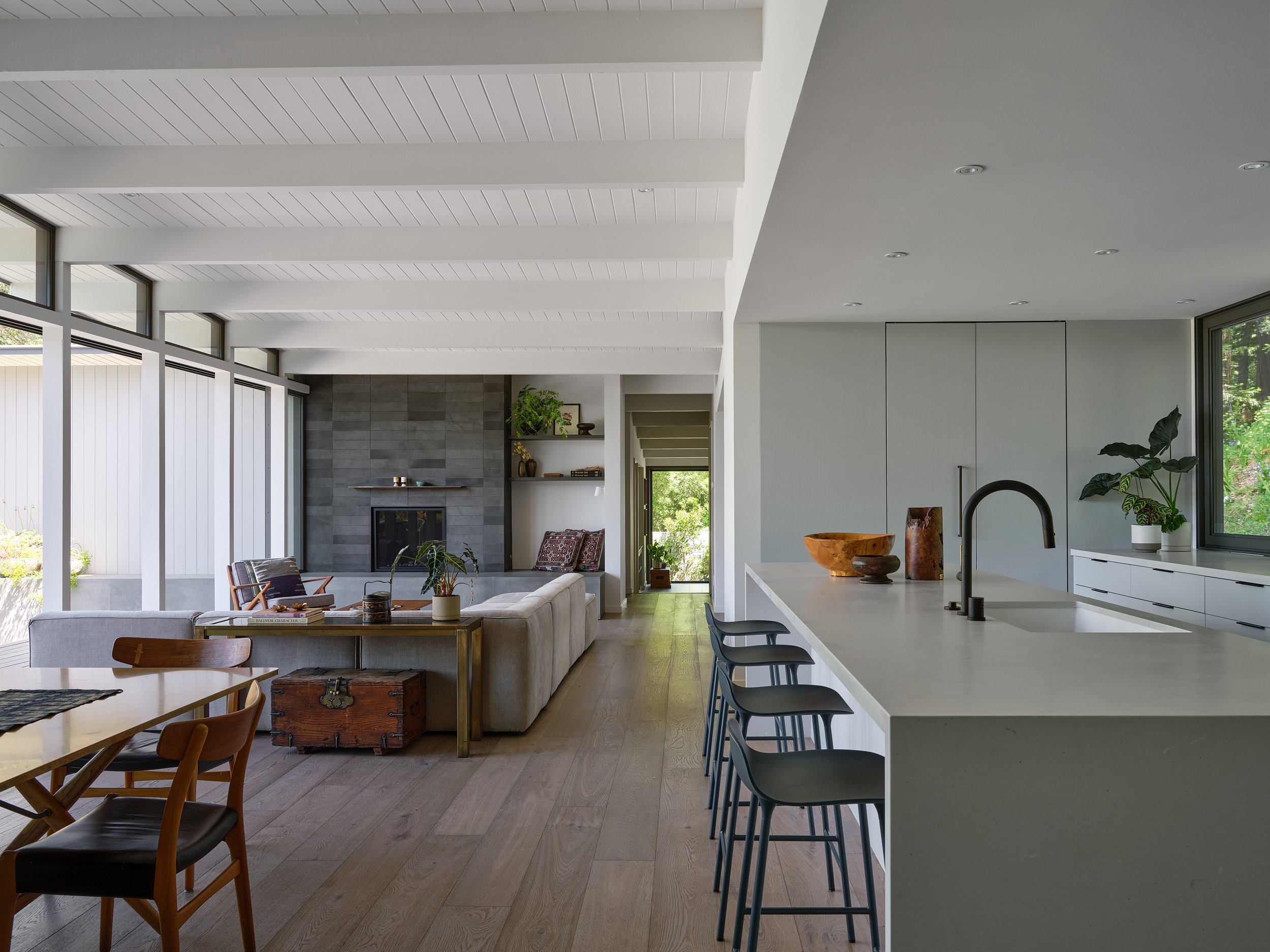 Open-concept living room and kitchen with modern design, large windows, wood flooring, white walls, and minimal decor.