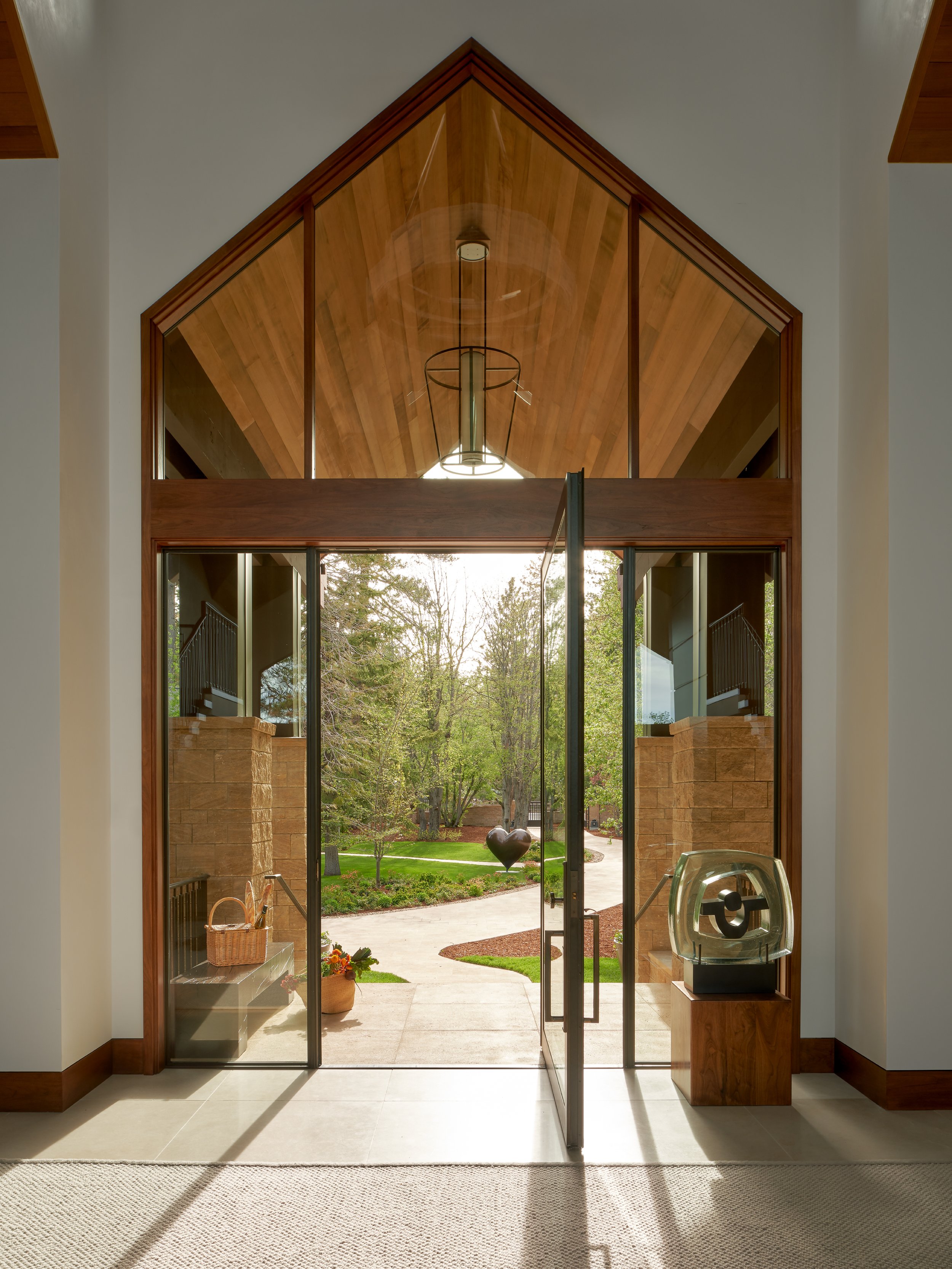 Interior view of a home's entrance door with glass panels, showing a landscaped yard outside with trees, flower pots, and a heart-shaped sculpture.