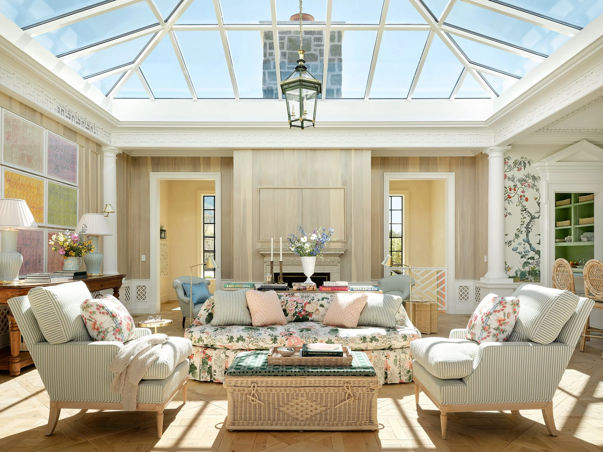 Bright living room with a glass ceiling, a fireplace, floral and striped furniture, and decorative accents.