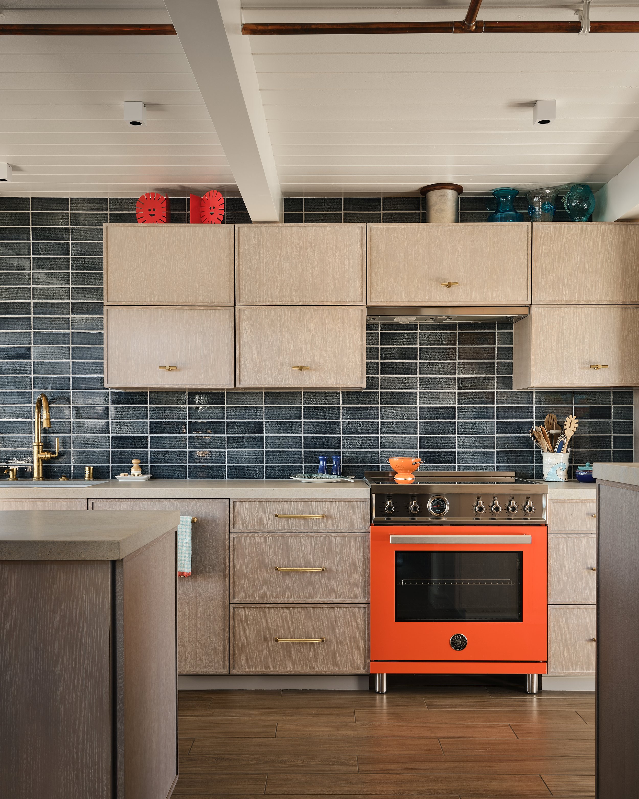 A modern kitchen with beige cabinets, black tile backsplash, and an orange stove.