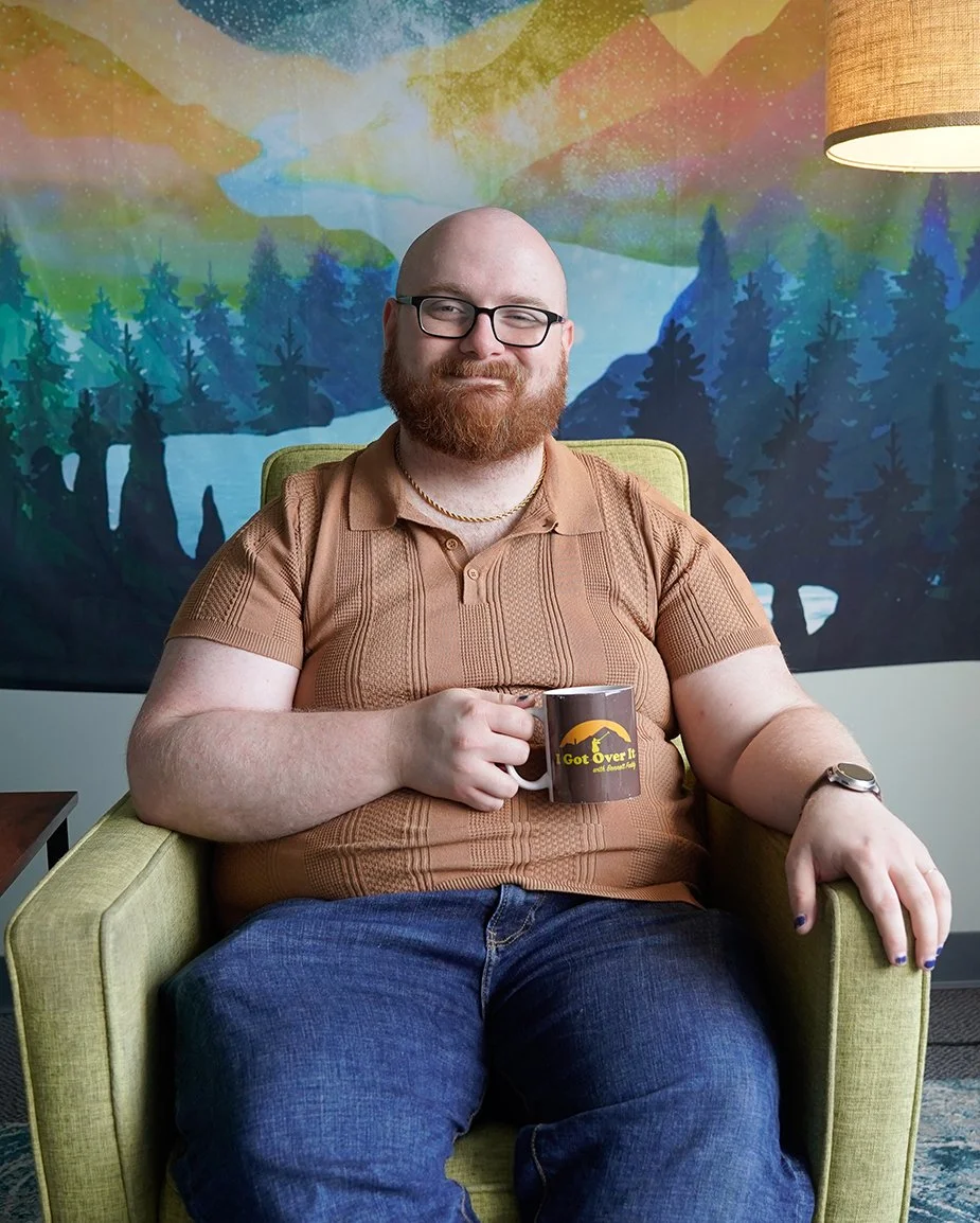 Sam DiMartino therapist in Nashville smiling with a mug sitting in a green chair with a colorful background