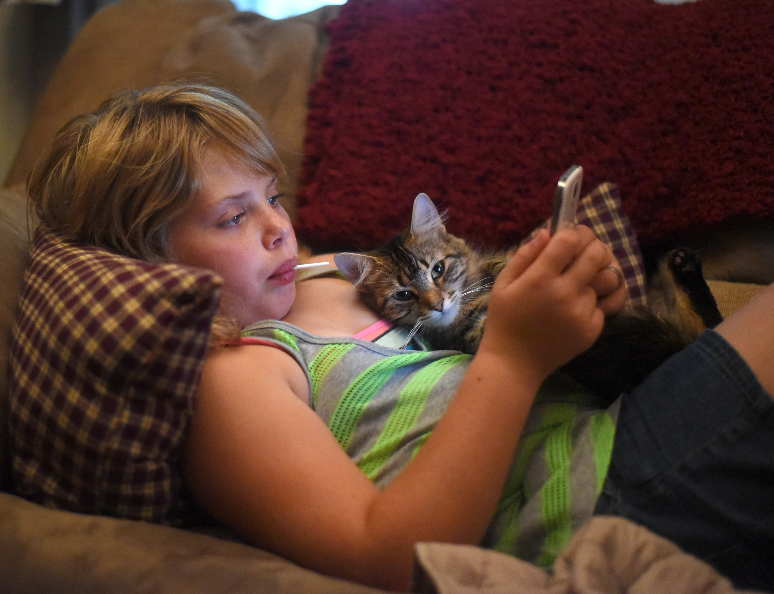  Nine-year-old Alivia Henning, who has autism, lays on her couch with her cat, Elsa, while playing on a cell phone at her home Sept. 22, 2016.&nbsp; 