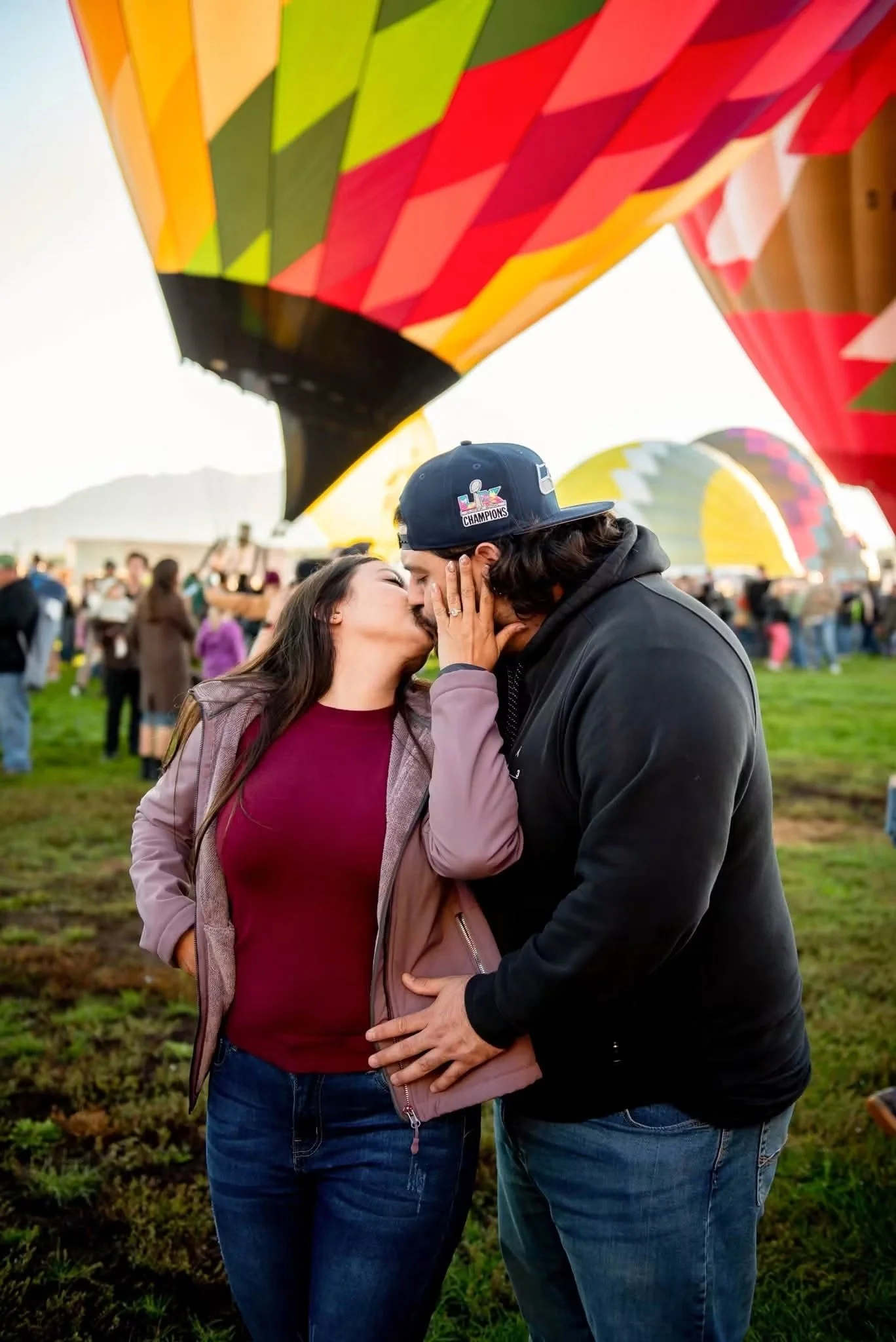Newly engaged couple kissing beneath a rainbow hot air balloon in Albuquerque