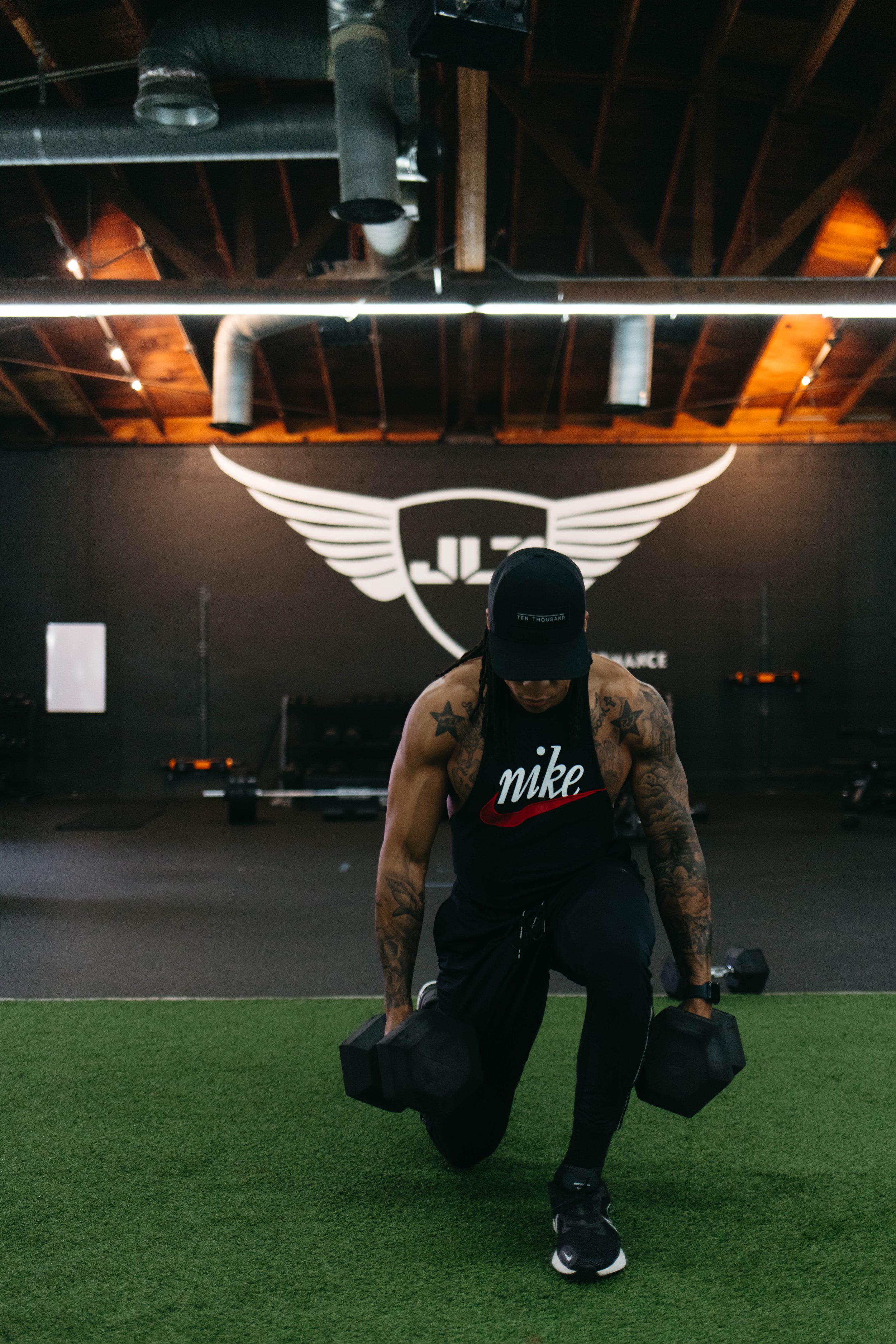Person exercising with dumbbells in a gym with a winged logo on the wall behind.