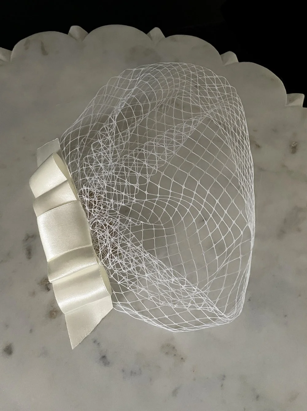 Close-up of cream white birdcage veil featuring flat satin bow and half face-framing net veil