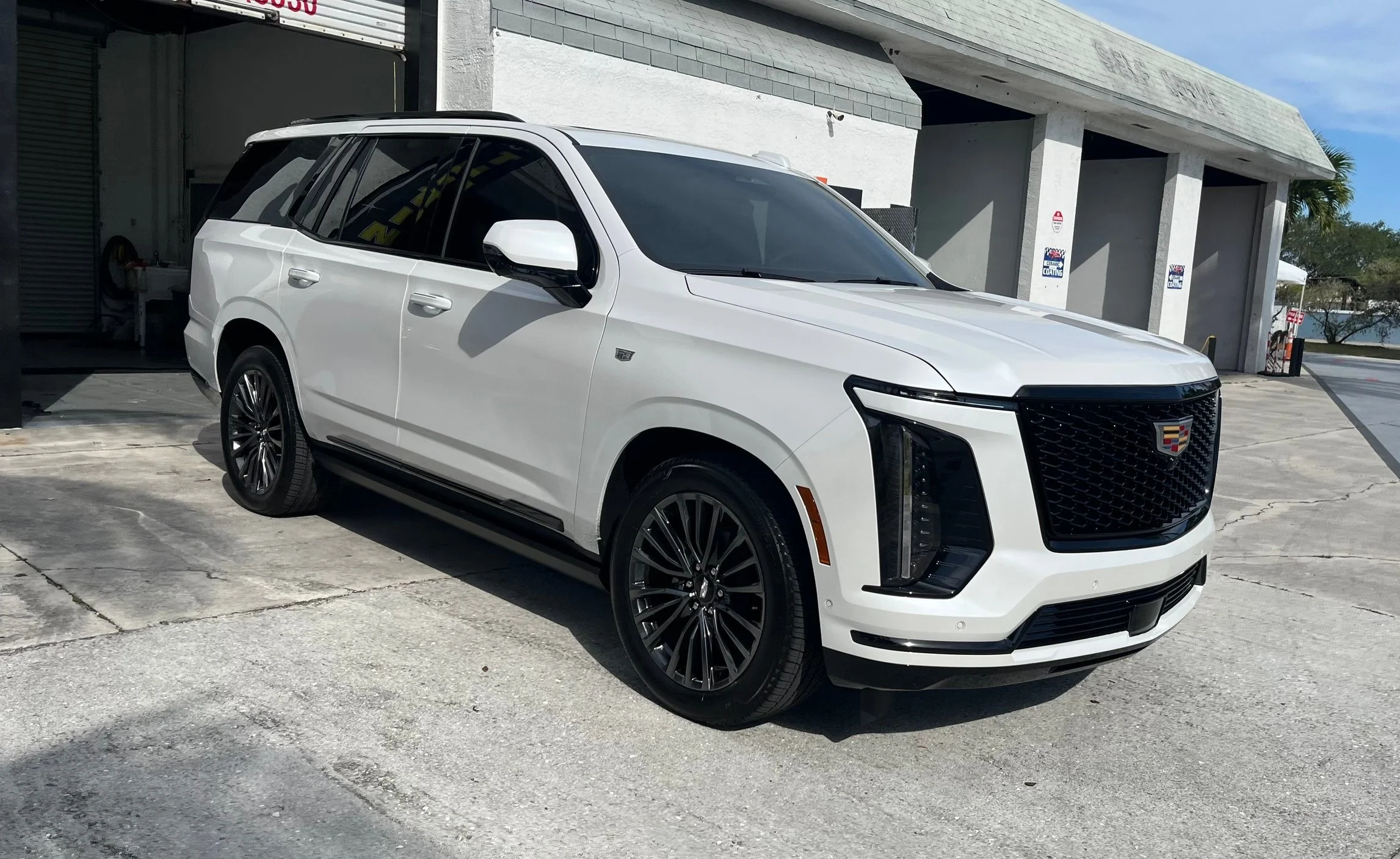 A white Cadillac SUV parked outside a building on a concrete surface with some cracks, under a partly cloudy sky.