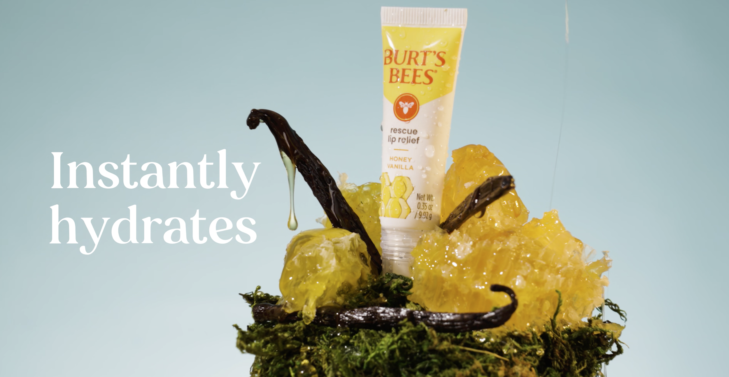 A Burt's Bees rescue lip balm tube placed on honeycomb and surrounded by honey and vanilla beans, with moss at the base, against a light blue background, with the text 'Instantly hydrates' overlayed.